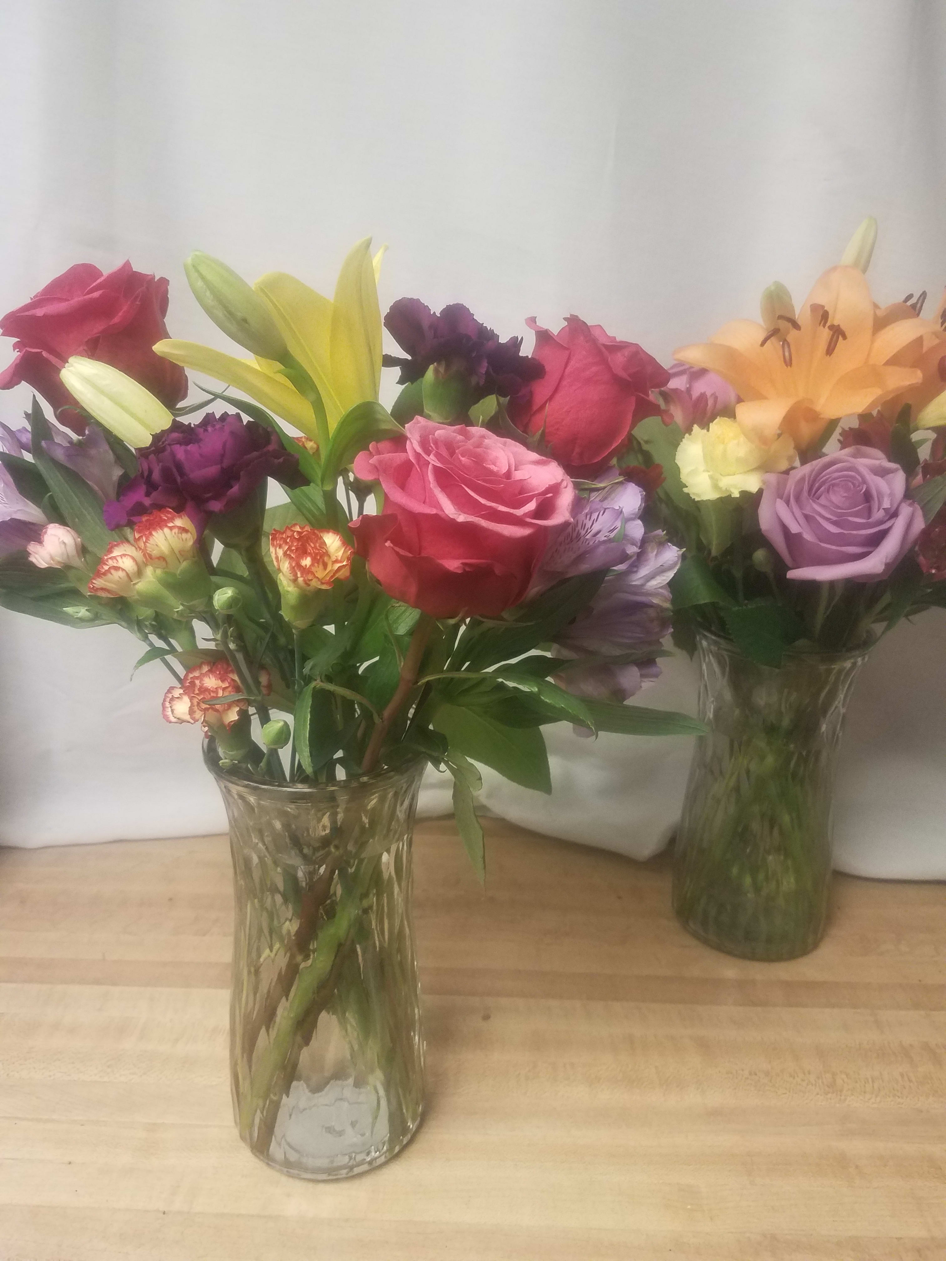 Two mixed flower bouquets in clear glass vases with roses and lilies