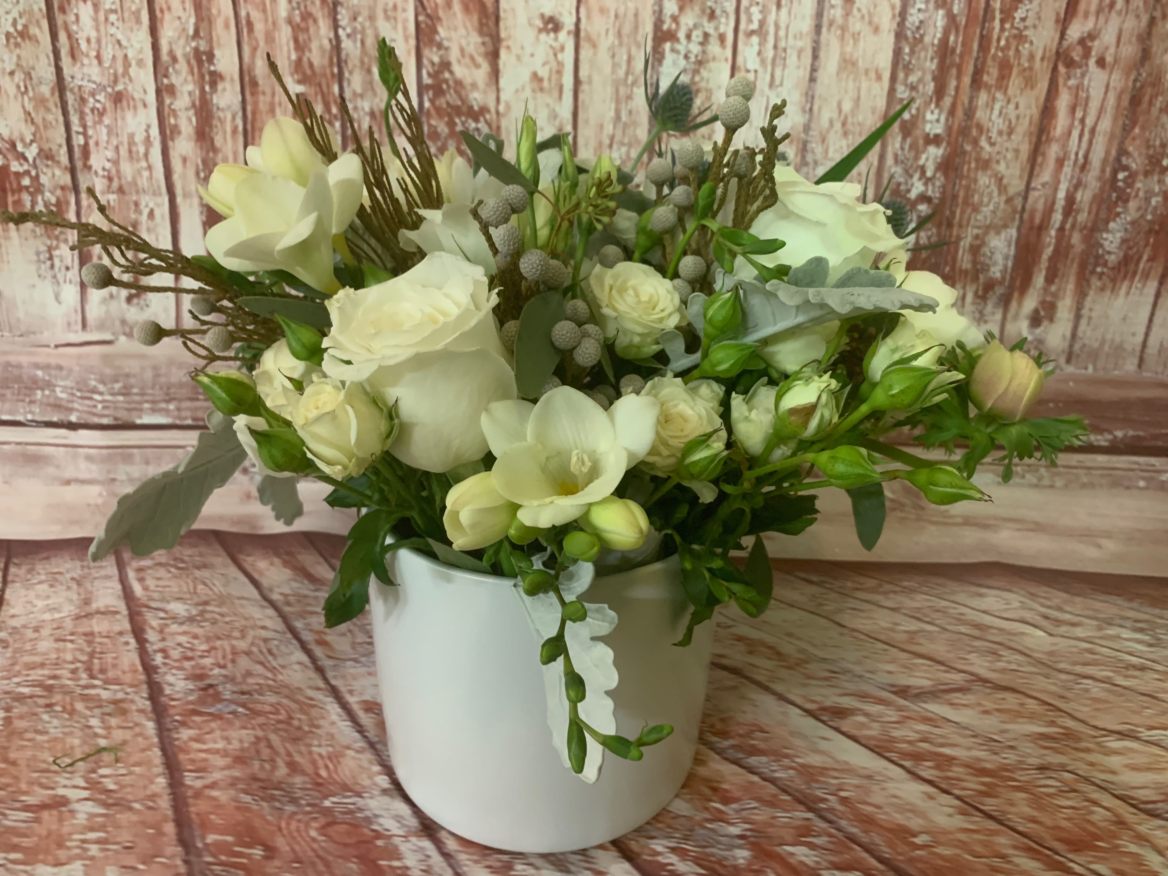 White floral arrangement in a white vase with roses and orchids