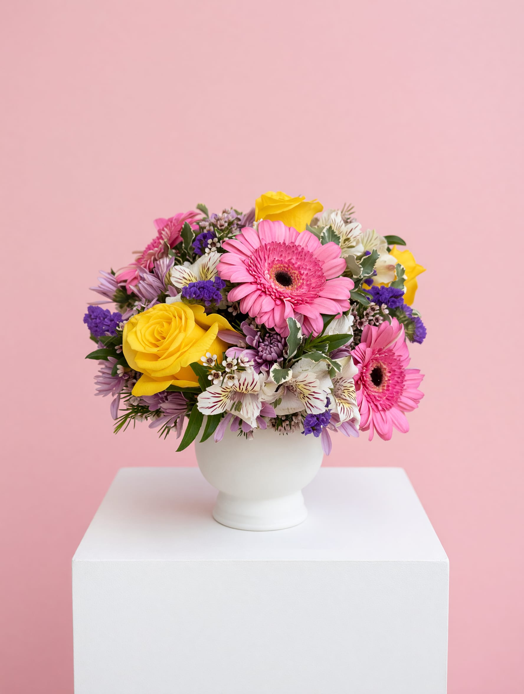 LF401 Morning Mom - This cheerful Mother's Day arrangement features a lovely mix of soft pink gerbera daisies, vibrant yellow roses, and delicate lavender chrysanthemums. Accented with purple statice and wax flowers, it's all beautifully arranged in a 5X5 white, ceramic compote for a sweet and charming presentation.  Perfect for celebrating the love, warmth and grace of every mom. 