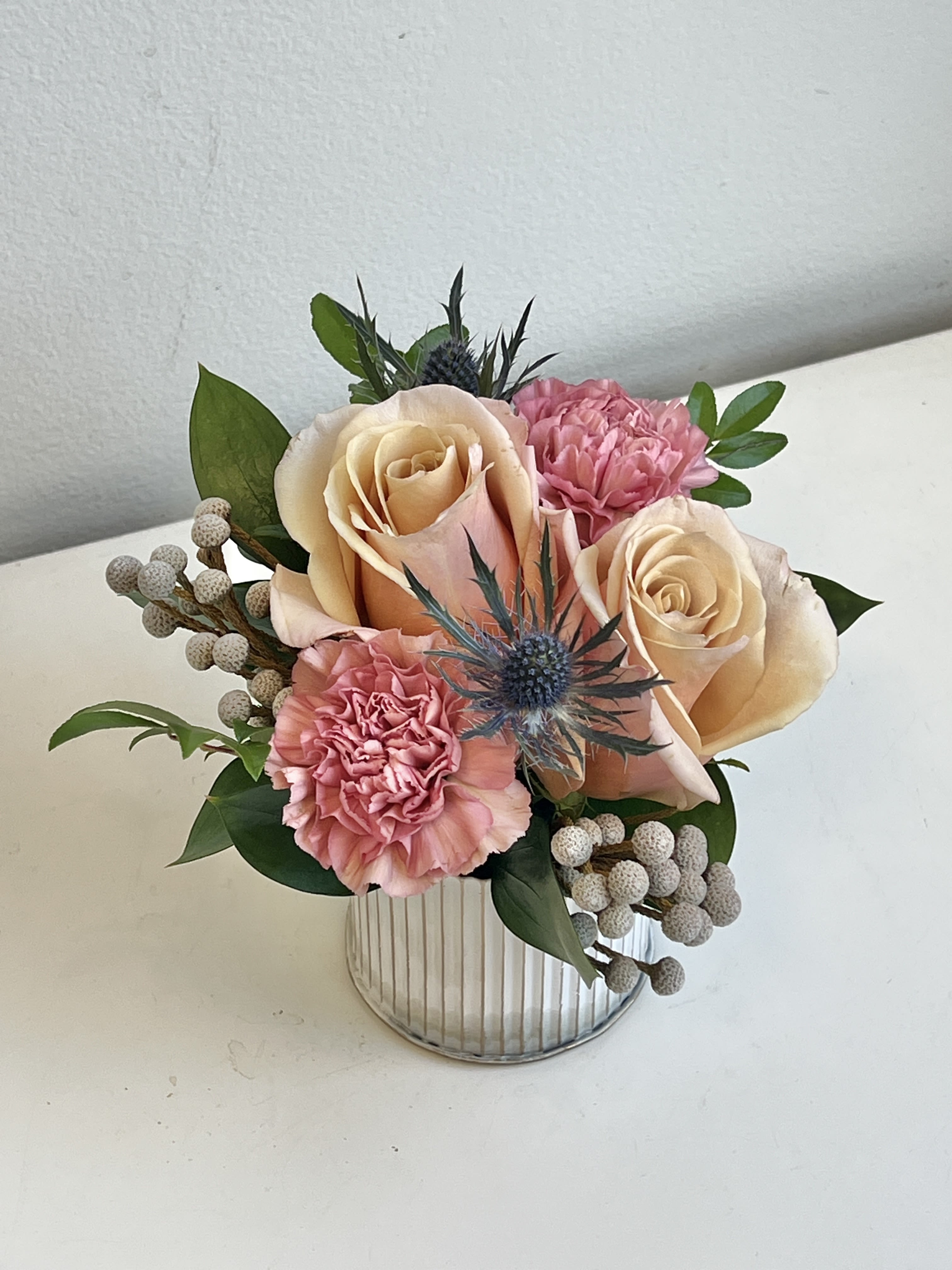 MD26-06 - A Combination of Light Pink Roses, Mauve/Pink Carnations, Blue Thistle and Silver Brunia Berries Designed in a Small White Tin Container.