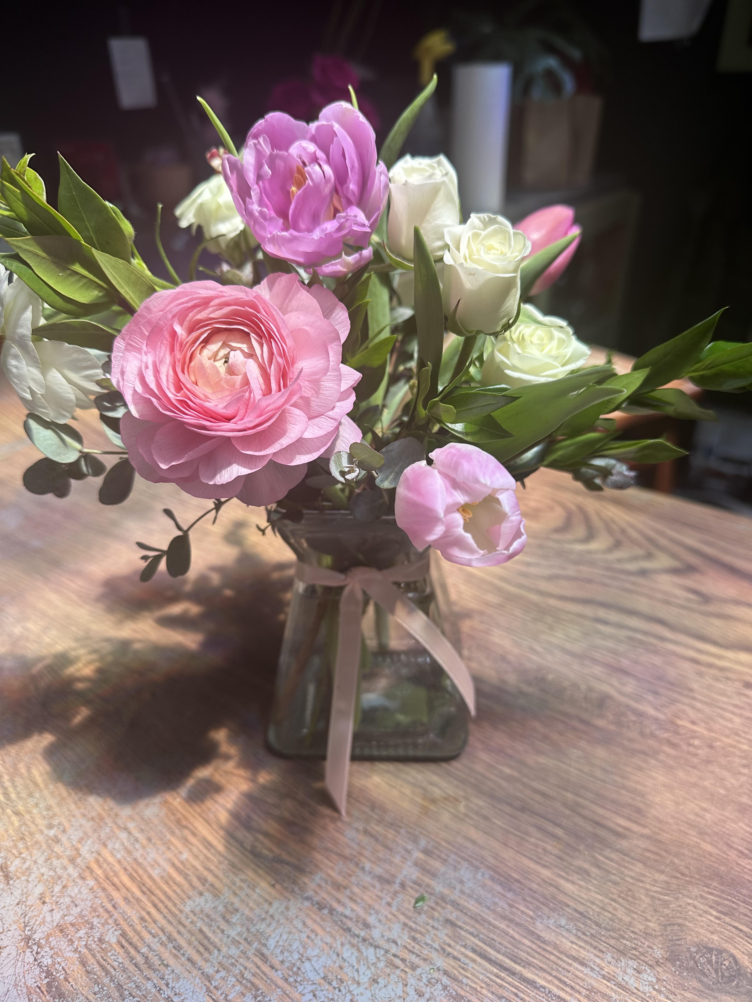 Made For Mom - A sweet, and darling arrangement made for all of the mothers in our lives, designed using lavender and pink tulips, white spray roses, blushy pink ranunculus, and white butterfly ranunculus, with textural foliage, all tied together with a light pink satin bow. 
