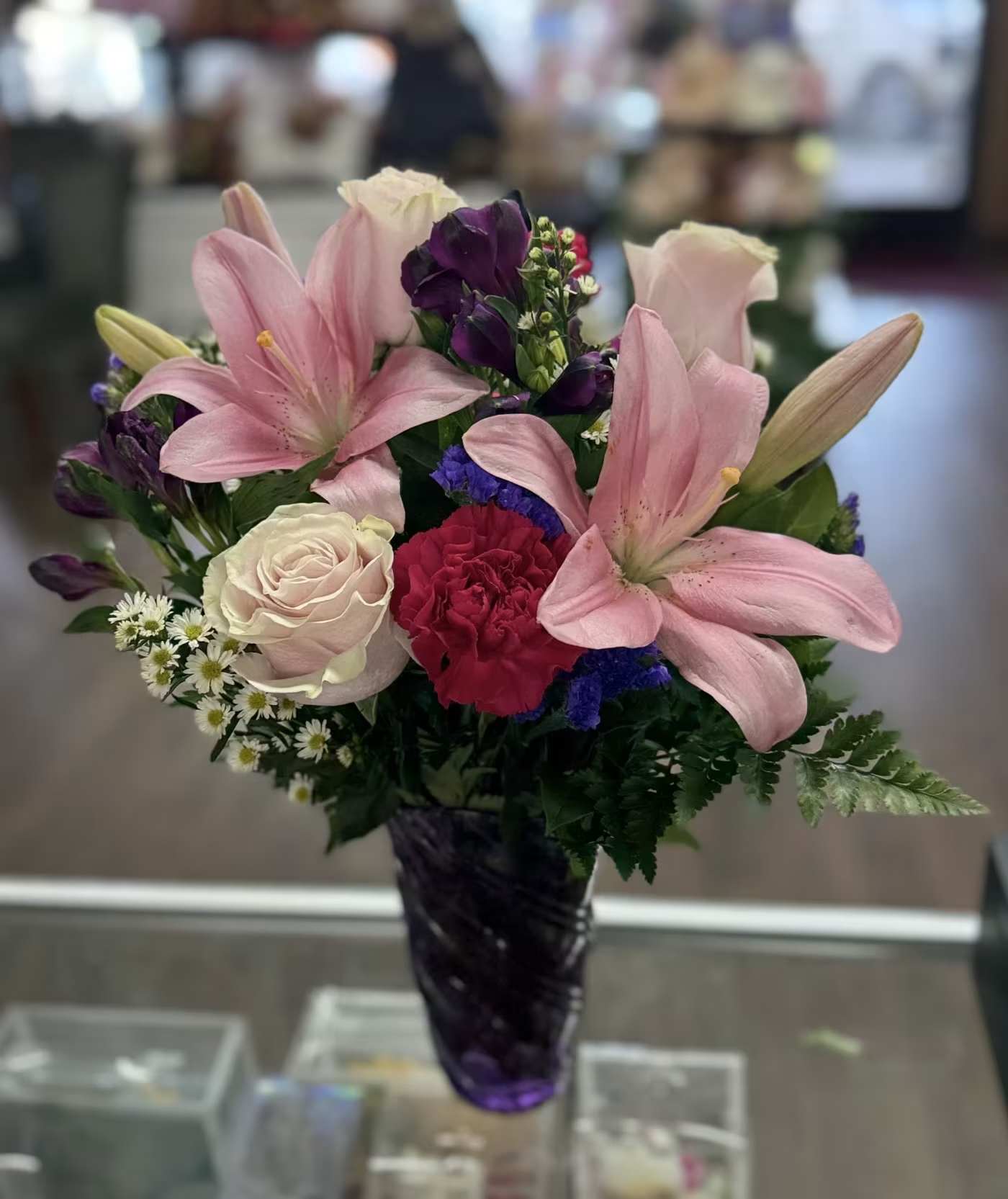 Once Upon A Bloom - Gathered mix of pink lilies, blush roses, carnations, alstroemeria and daisies in a purple glass vase.  