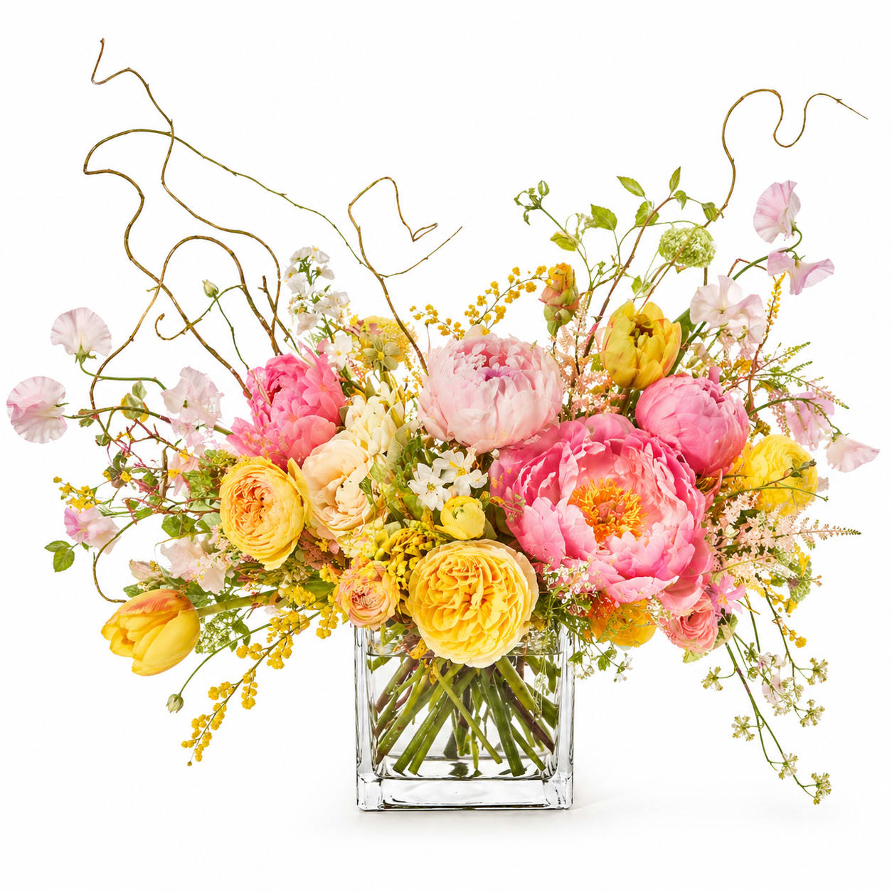 The Golden Hour Peony Cube - A vibrant, whimsical garden-style arrangement featuring lush peonies in pink tones paired with sunny yellow blooms and delicate seasonal accents in a clear glass cube.
