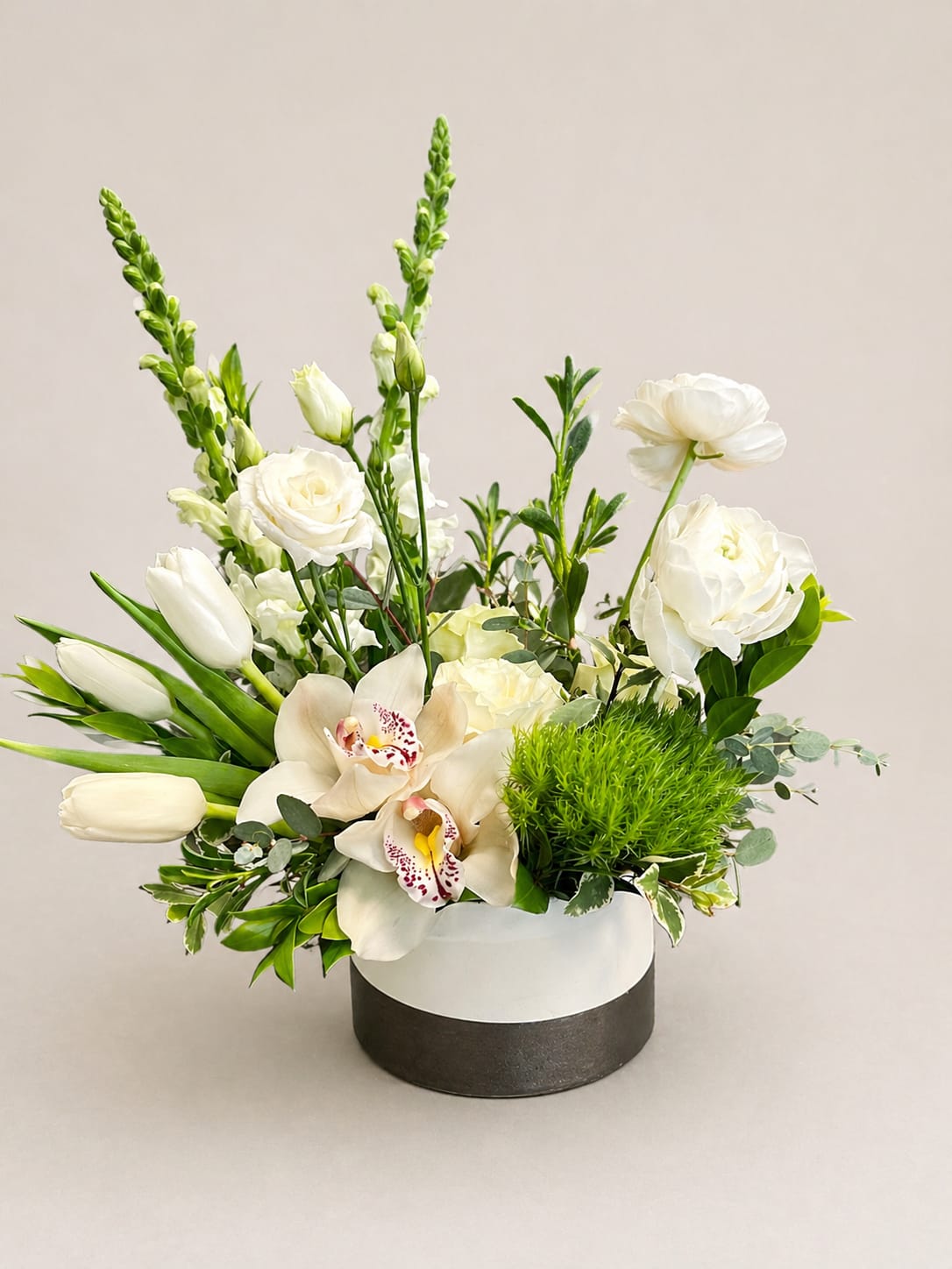 Grace in Bloom  - This compact design uses layered blooms and varied heights-rounded tulips and roses set against sculptural orchids and upright snapdragons-to give texture and depth in a neat, box-style container. The low-profile container keeps the arrangement feeling modern and gift-ready, making it easy to present right out of the shop.