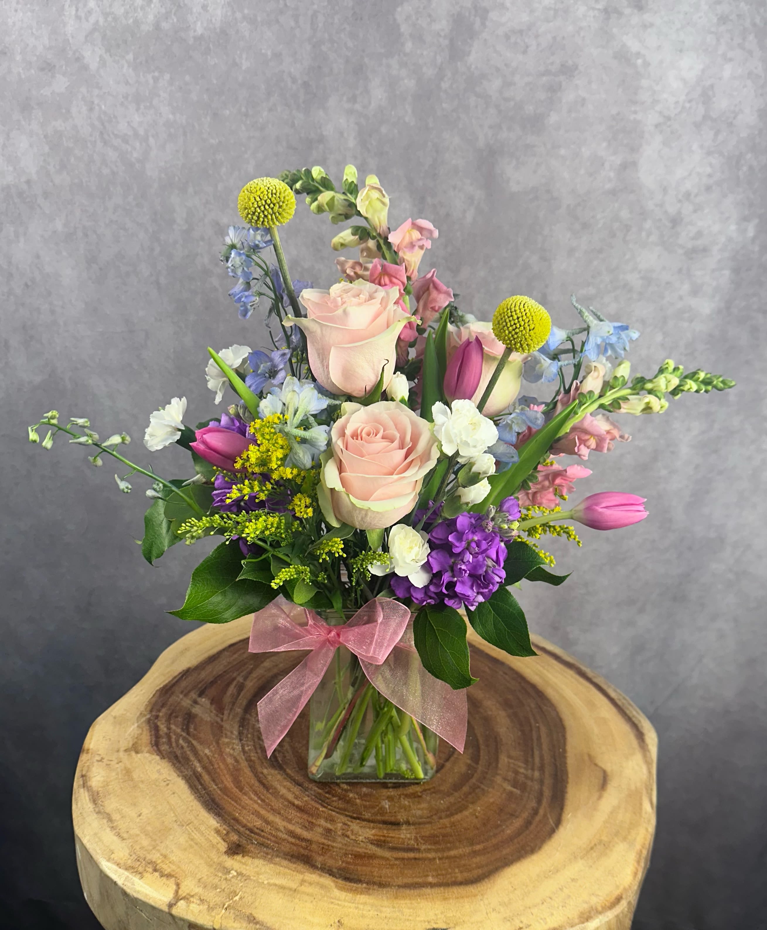 Cottage Charms - Soft, airy, and full of garden beauty, Cottage Charms is a front-facing, one-sided arrangement inspired by the ease of a blooming countryside garden. Includes roses, stock, snapdragons, delphinium, billy balls, and pixie carnations. This arrangement stands approximately  14" high and 10" wide.  Please Note: Standard Delivery for this product occurs in the afternoon, between 2:30pm and 7pm. If you need it by a certain time, there is an option to select a timed window for scheduled deliveries.