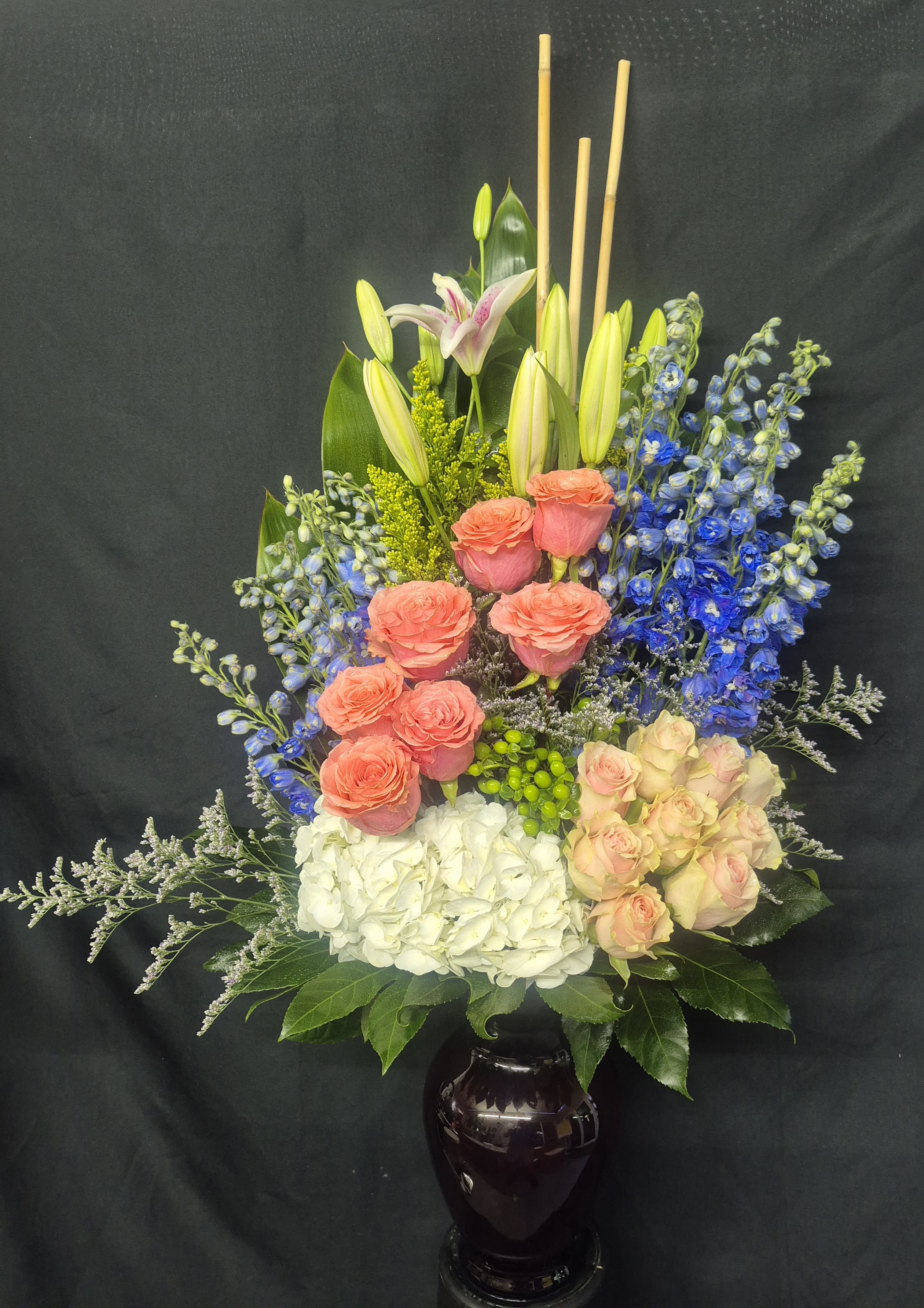 THE CELESTINO - A TALL AN ELEGANT DESIGN FEATURING PINK STARGAZER LILLIES, BLUE DELPHINIUMS, GREEN HYPERICUM BERRIES, WHITE HYDRANGEAS, PEACH AND PINK ROSES. YELLOW SOLIDAGO AND WHITE CASPIA FILLER. I PERFECT ARRANGEMENT TO SEND TO CELEBRATE A BIRTHDAY OR A HAPPY EVENT.
