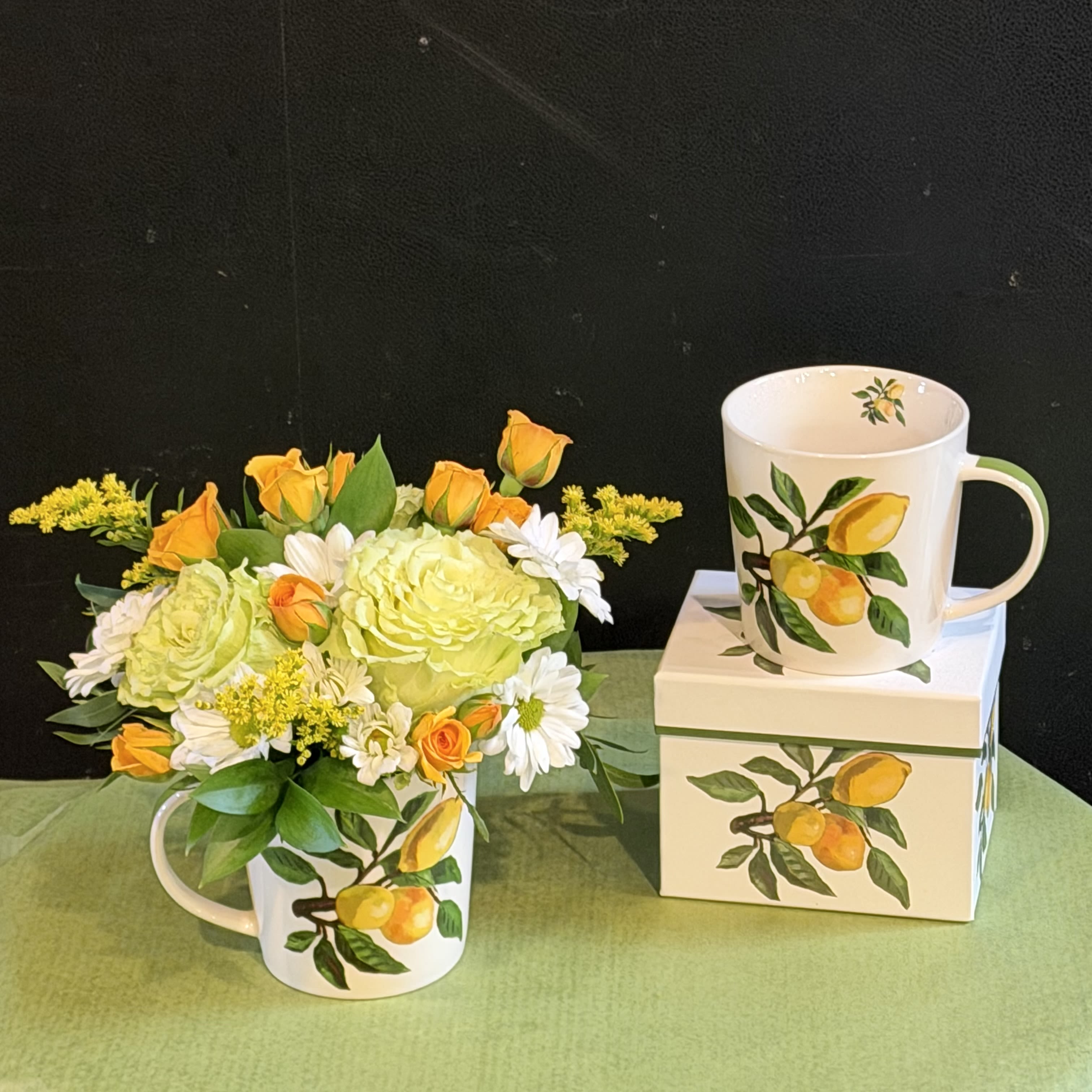 Lemon Mug - Bright and refreshing floral arrangement in a charming lemon-print mug. Features soft greens, whites, and yellow blooms. Mug is microwave and dishwasher safe—perfect as a keepsake after the flowers.  
