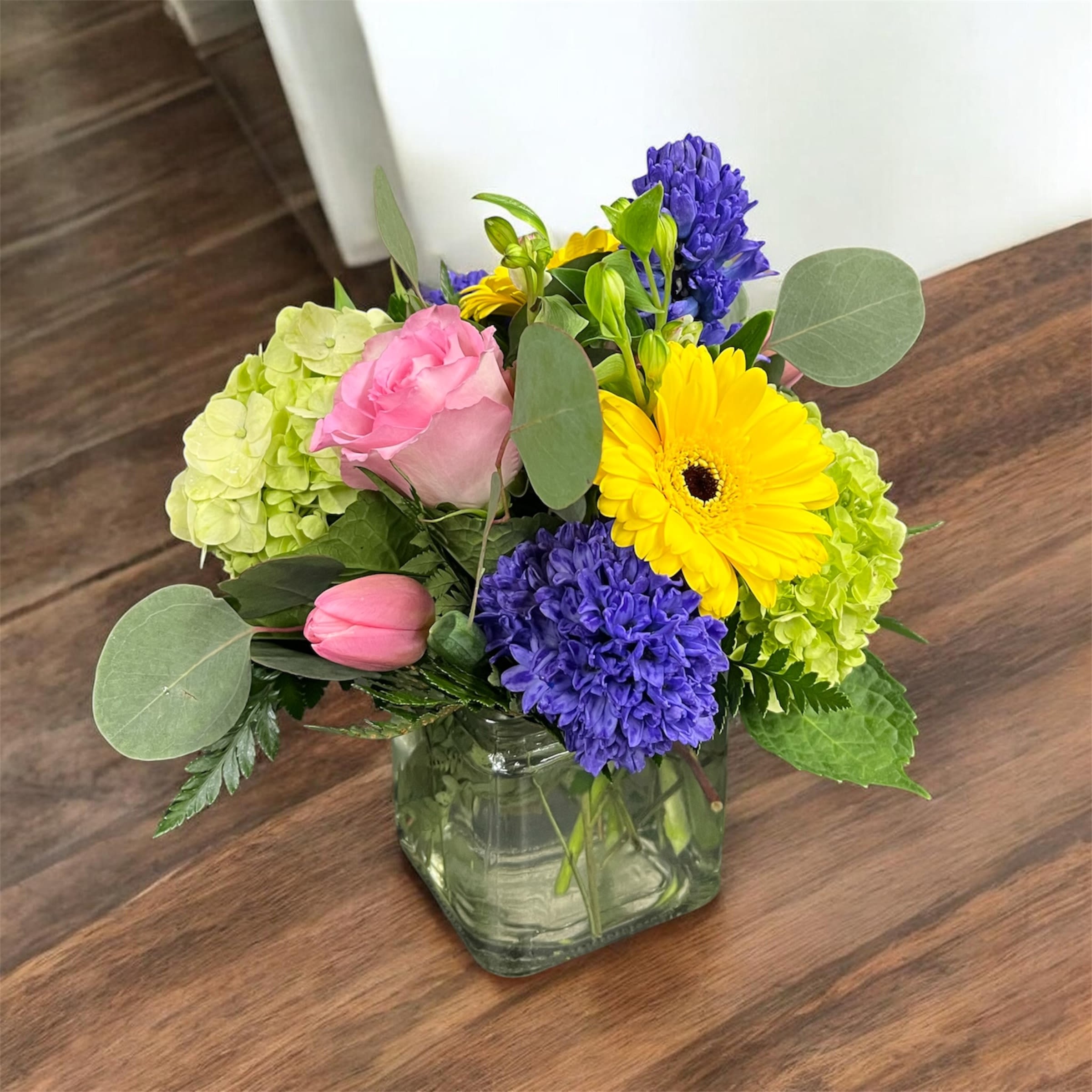 Designers Choice Cube Arrangement  - A compact flower arrangement in a cube vase features a neat, modern design with blooms trimmed to a low height, forming a tight, rounded shape. 