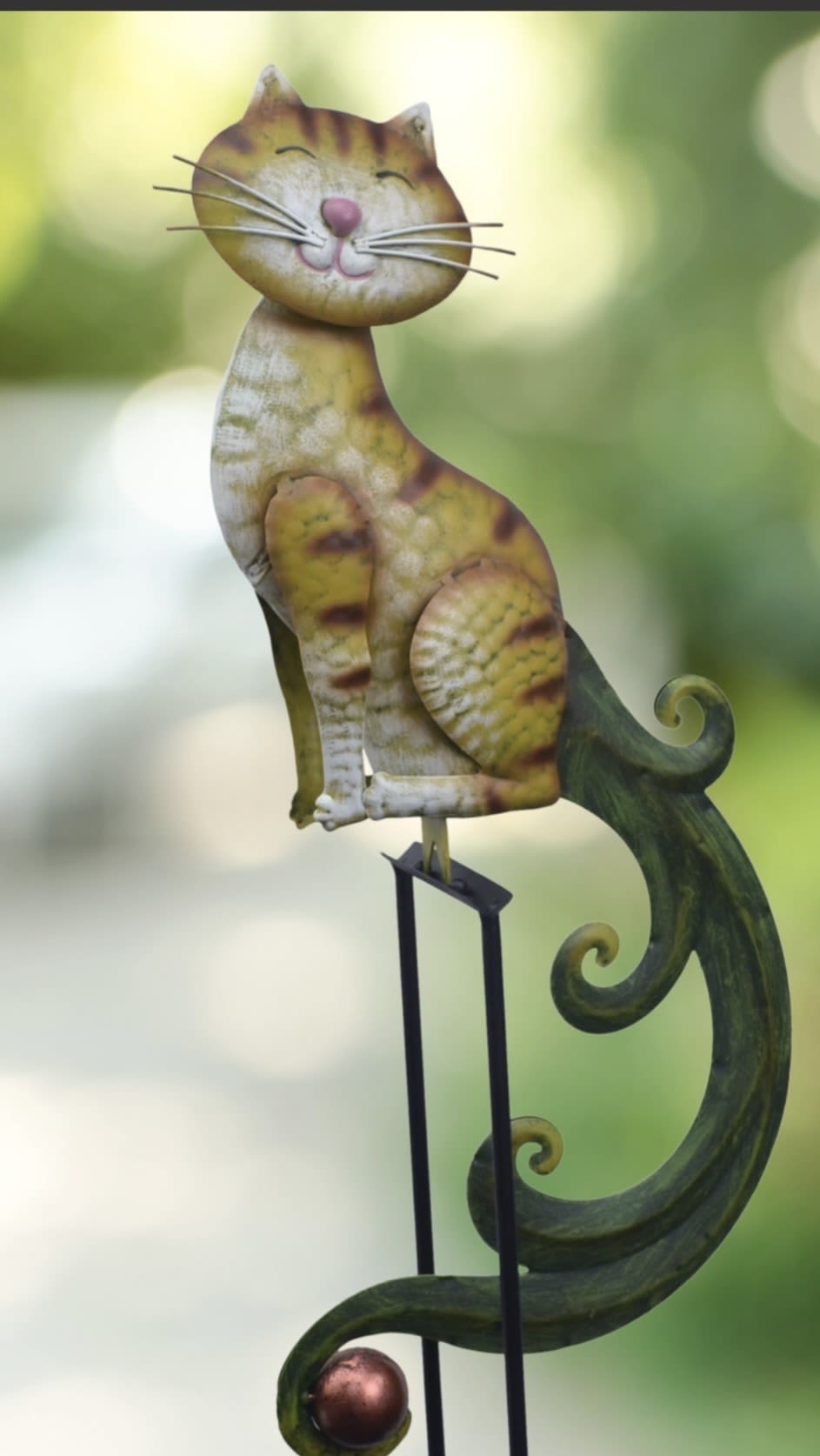 Smiling Cat Yard Rocker - A playful handcrafted cat figurine on a slender black metal stand makes an unexpected gift for cat lovers and anyone who enjoys whimsical home décor. This decorative accent - ideal for birthdays, housewarmings, or as a cheerful "thinking of you" surprise - brings a touch of garden-art charm to tabletops, shelves, or entryway consoles.  The figurine features a textured, hand-painted body in mottled yellow, white, and brown tones with a curled green tail and small pink facial details that catch the eye. Mounted on a slim metal stand, it stands upright to add vertical interest without taking up much space; the lightweight construction makes it easy to move where your recipient will enjoy it most.  Give it to someone who appreciates quirky, artisan-style accents-the kind of piece that makes them smile every time they pass it. Care is simple: dust lightly with a soft cloth and avoid prolonged outdoor exposure to preserve the painted finish.