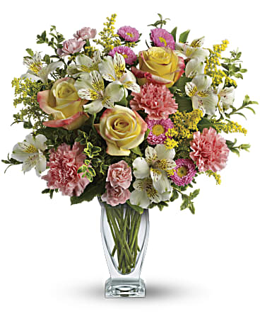 Mixed bouquet of roses, carnations, alstroemeria, and yellow filler flowers in a glass vase