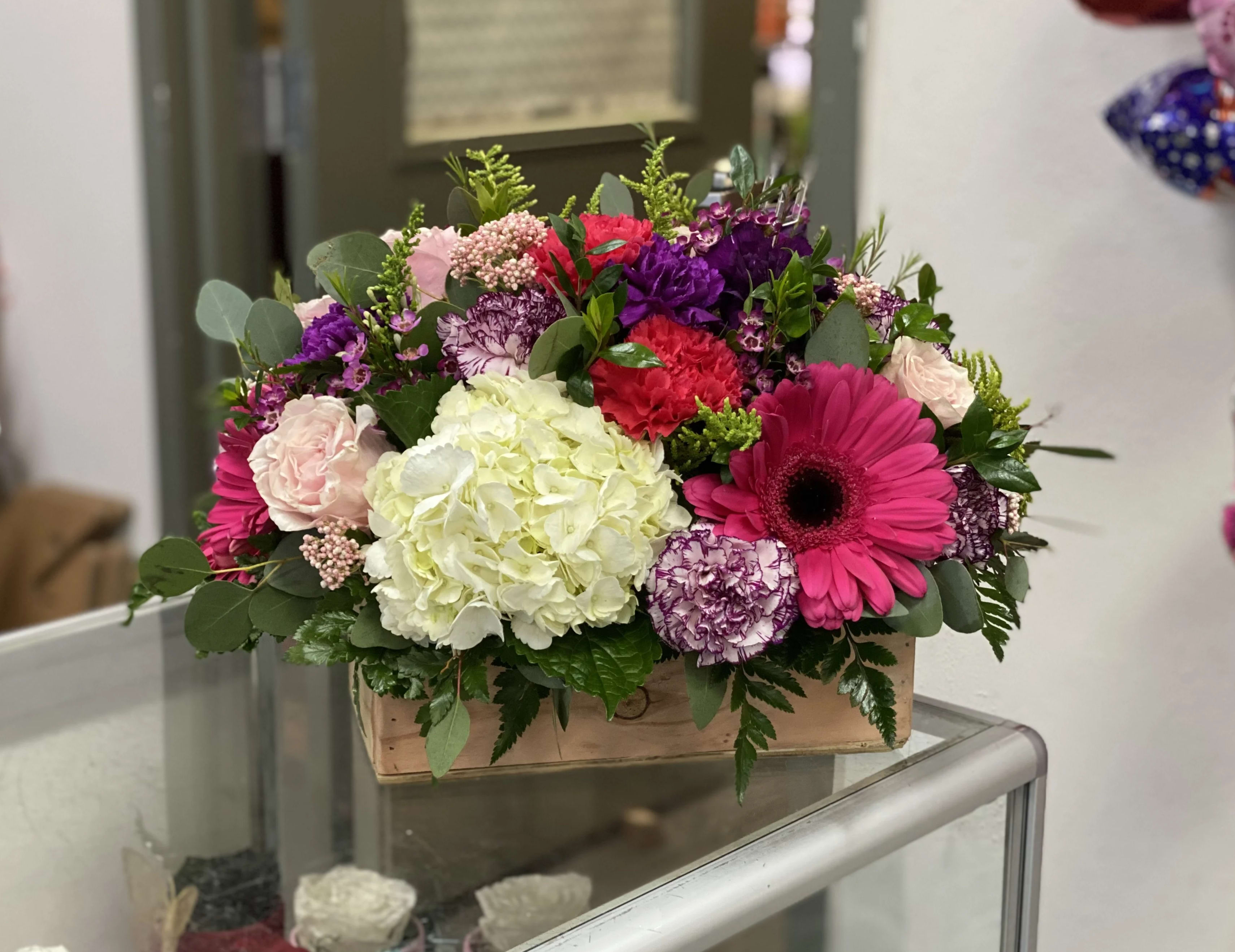 Mixed bouquet in a wooden box with pink, purple, white, and red flowers
