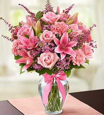Pink roses and lilies arranged in a clear glass vase with a pink ribbon