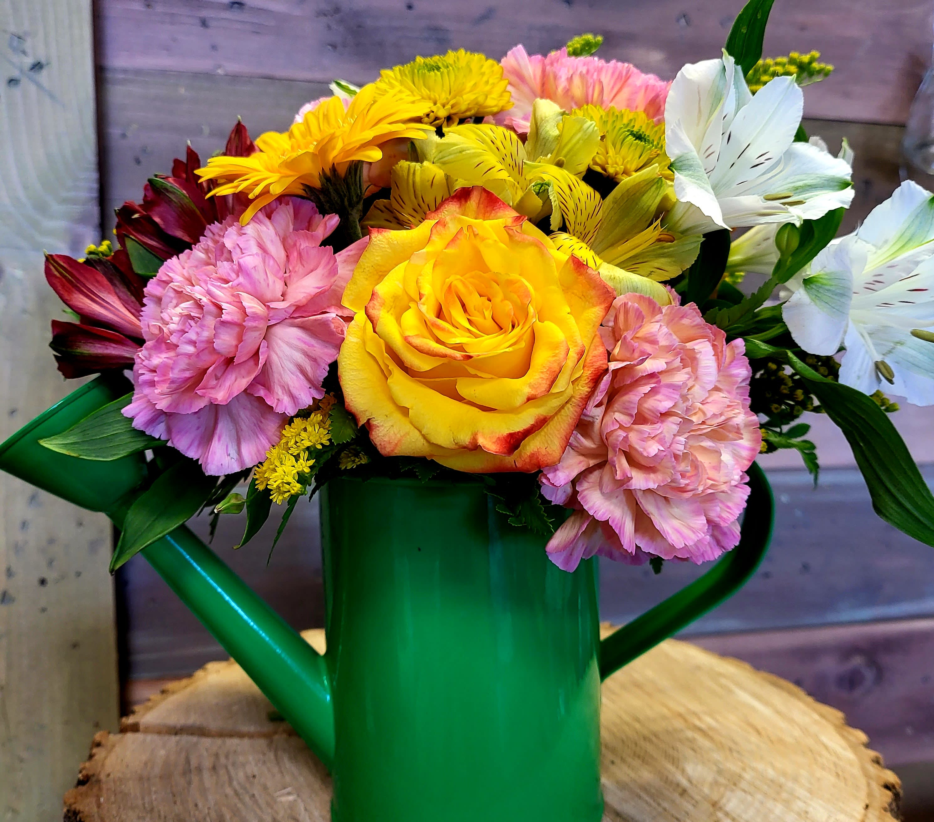 Cheerful mixed bouquet of yellow rose, pink carnations and white lilies in a green watering can