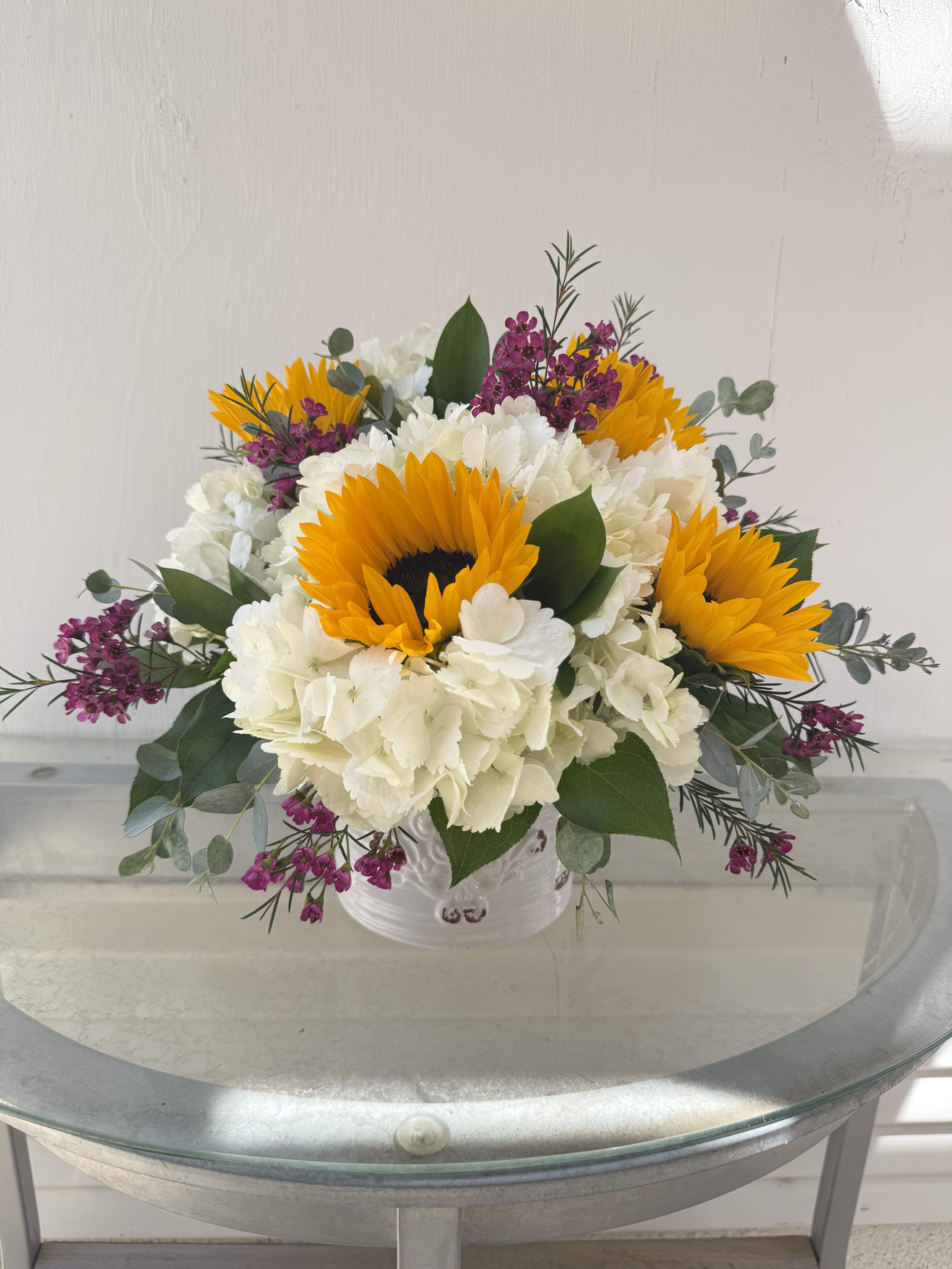 Sunny Smiles for Mom - This cheerful arrangement radiates warmth and brightness with its sunny, inviting palette. Bold golden sunflowers take center stage, their rich, dark centers creating a striking contrast against soft, cloud-like clusters of white hydrangea. The combination feels both fresh and uplifting.