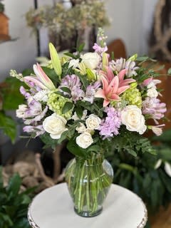 Mother's Garden Embrace - A lush, garden-inspired arrangement featuring pink lilies, creamy white roses, soft lavender accents, and green hydrangeas. Designed in a classic glass vase, this piece feels airy and full of life just like Mom deserves.