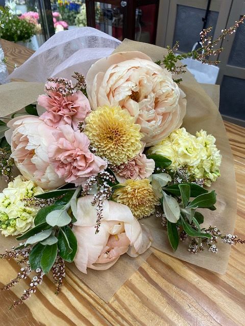 Pastel bouquet with large blush peonies and yellow blooms wrapped in paper