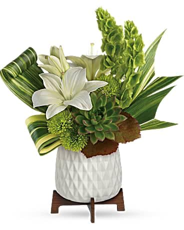 White lilies and green tropical foliage in a white vase