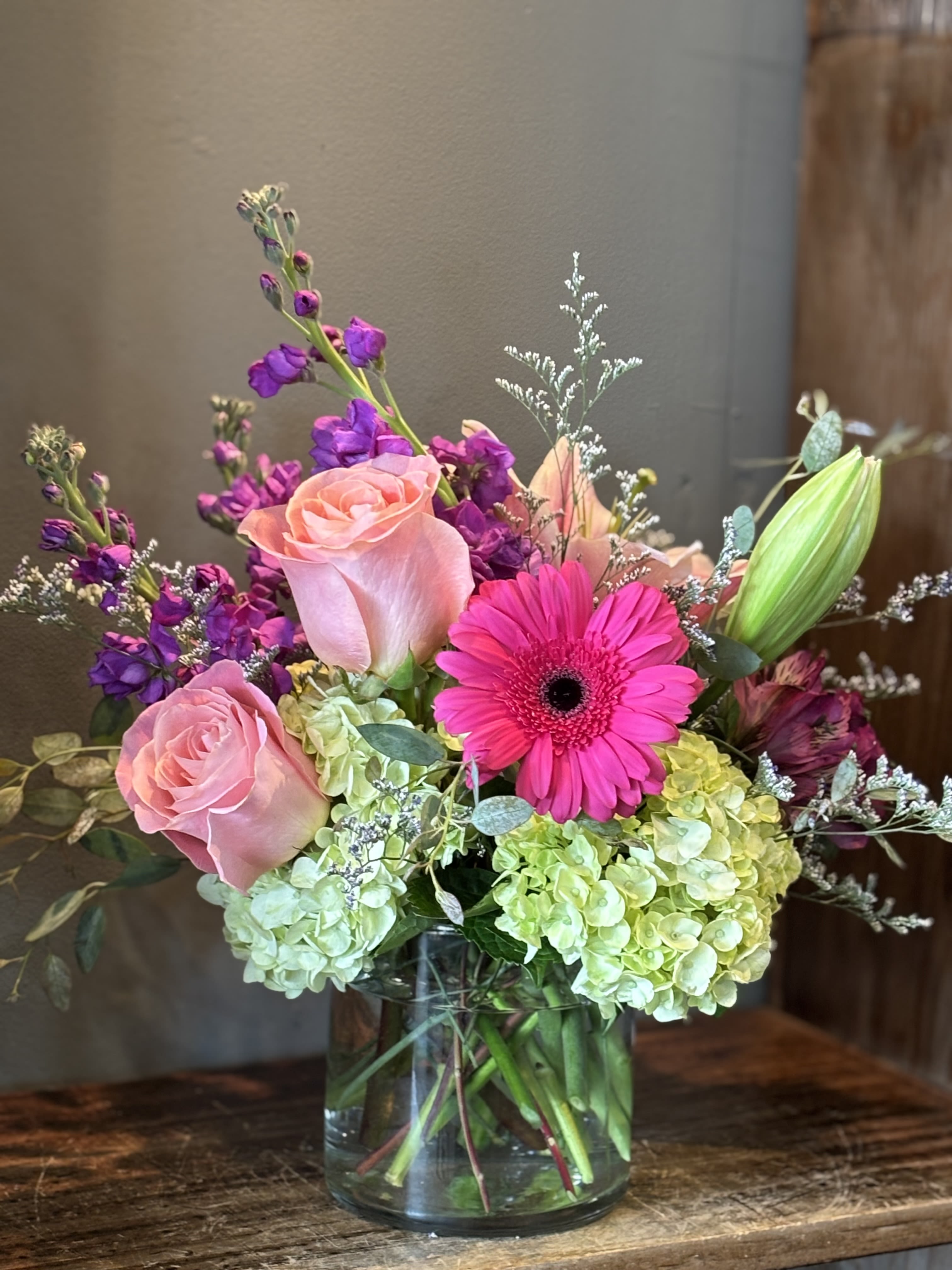 Mixed bouquet of pink roses, hot pink gerbera, purple flowers and green hydrangeas in a clear glass vase