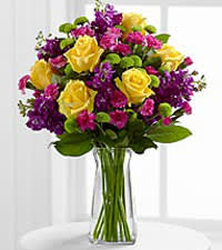 Bouquet of yellow roses and purple flowers in a clear glass vase