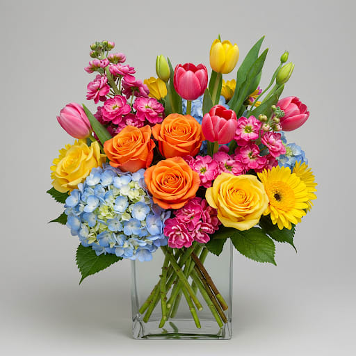 Mixed bouquet in a clear glass vase with roses, tulips, hydrangea, and daisies