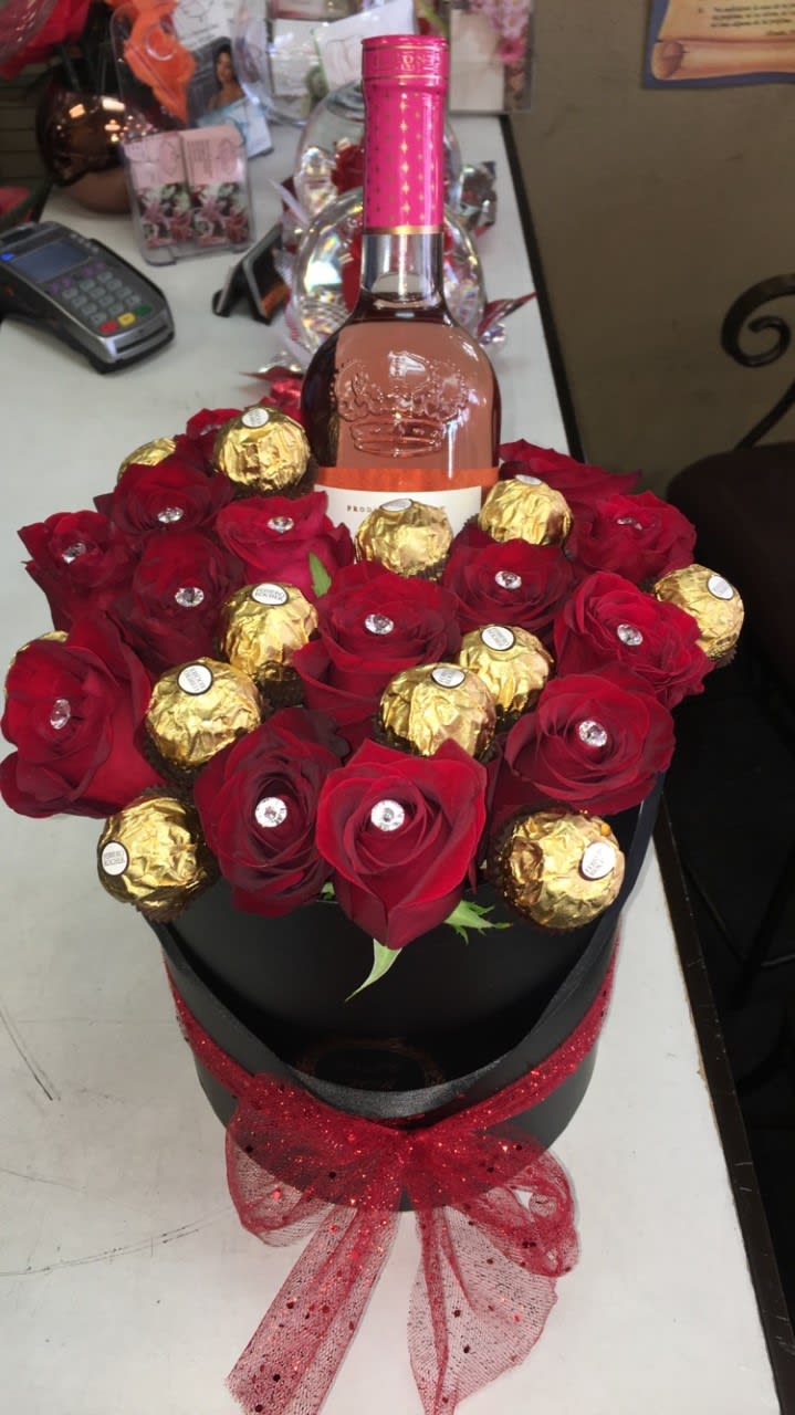 Red roses and gold-wrapped chocolates arranged around a wine bottle in a black box