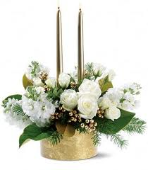 White floral arrangement in a gold container with two tall candles