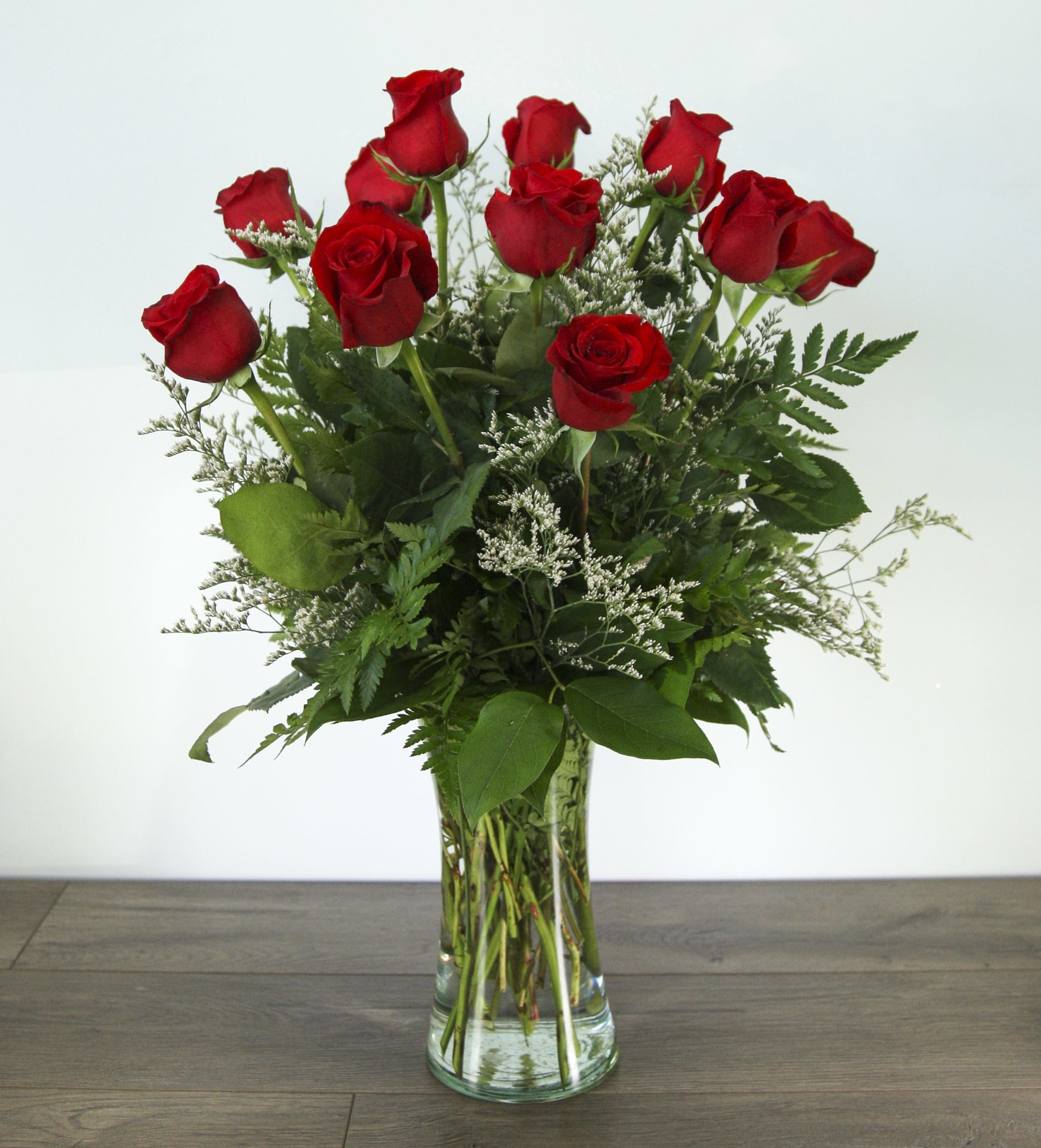 Red roses arranged in a clear glass vase with greenery