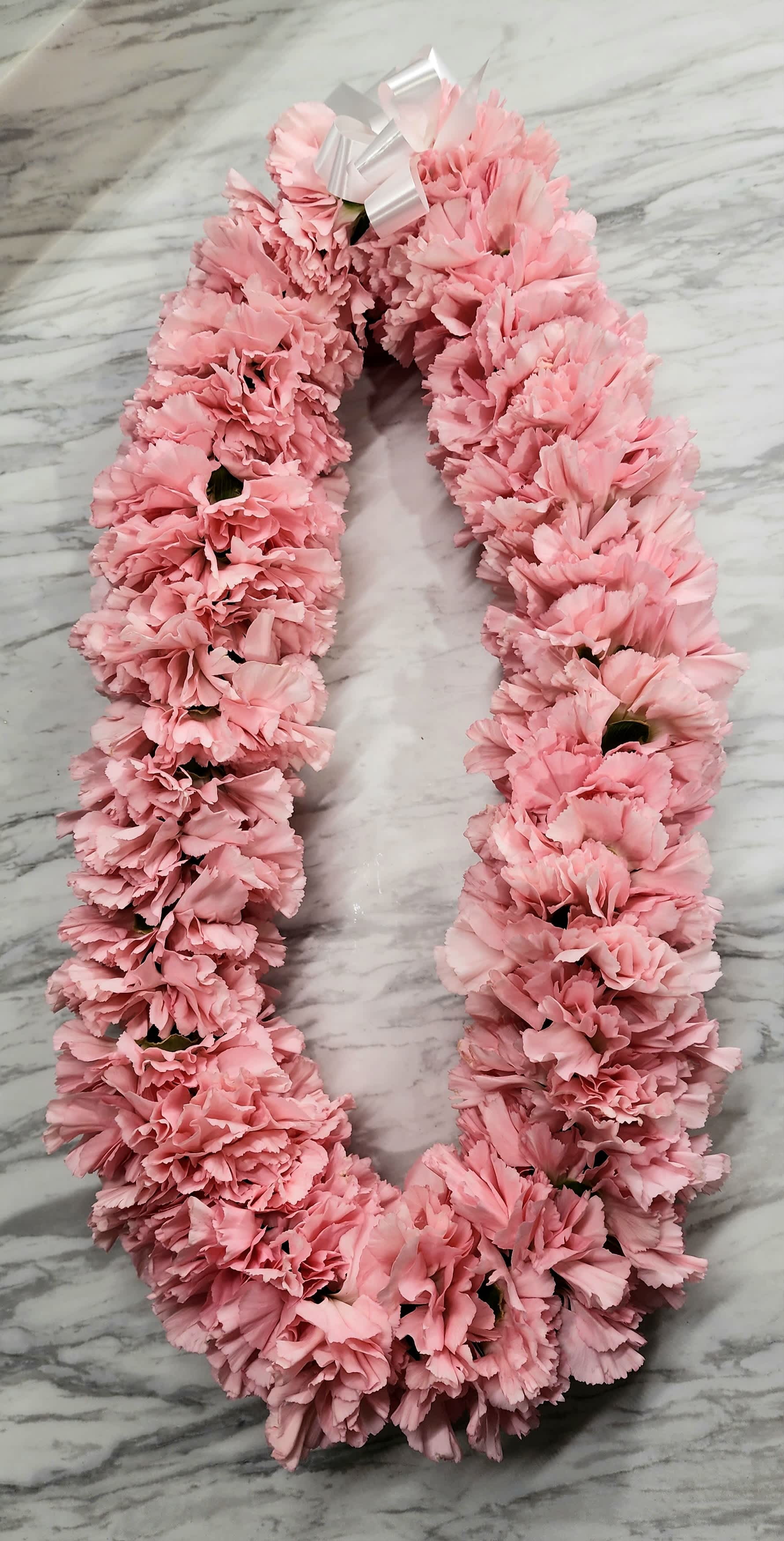 Pink carnation lei with a white ribbon bow