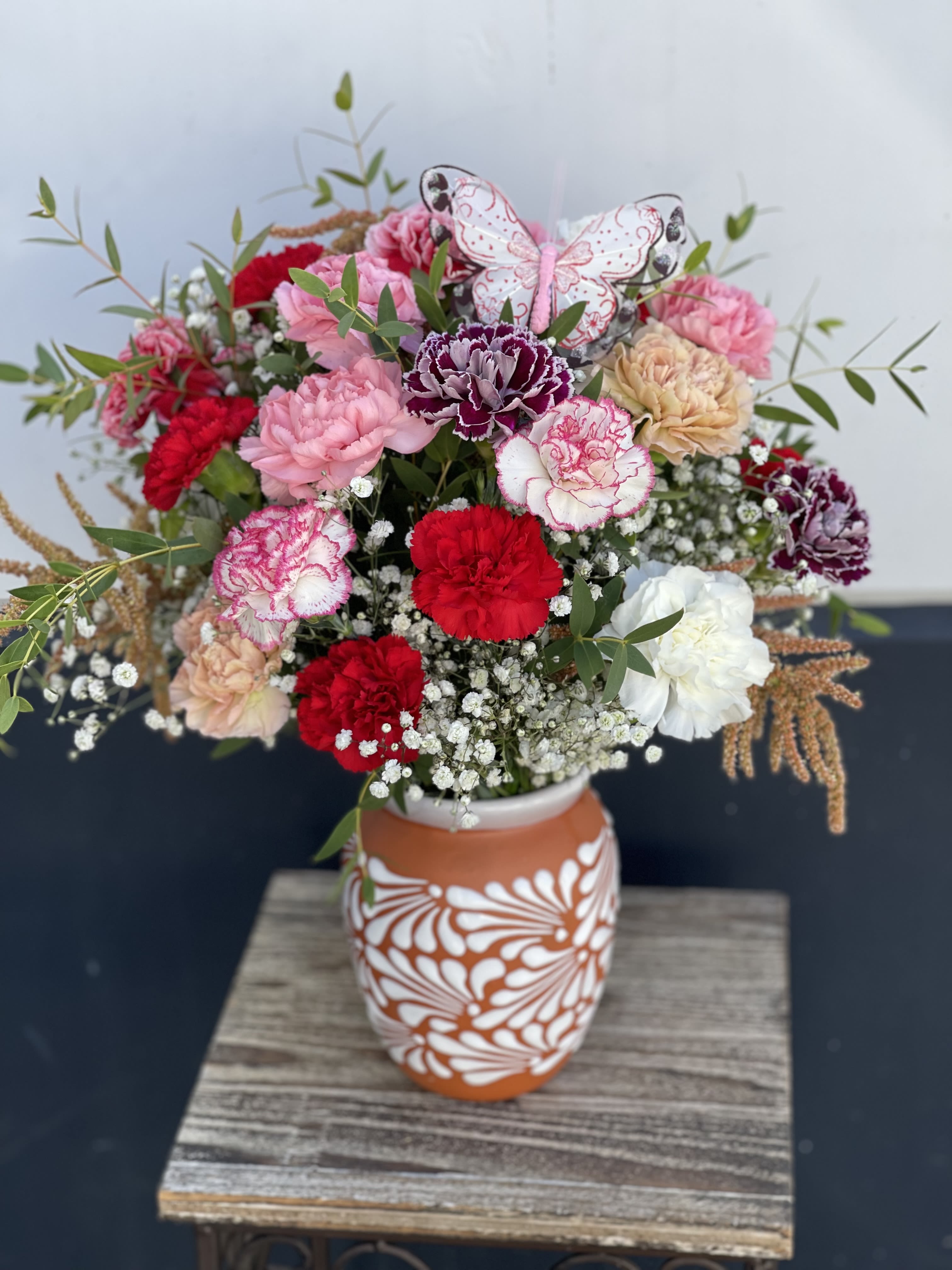 Mixed bouquet of carnations in a patterned vase with a butterfly decoration
