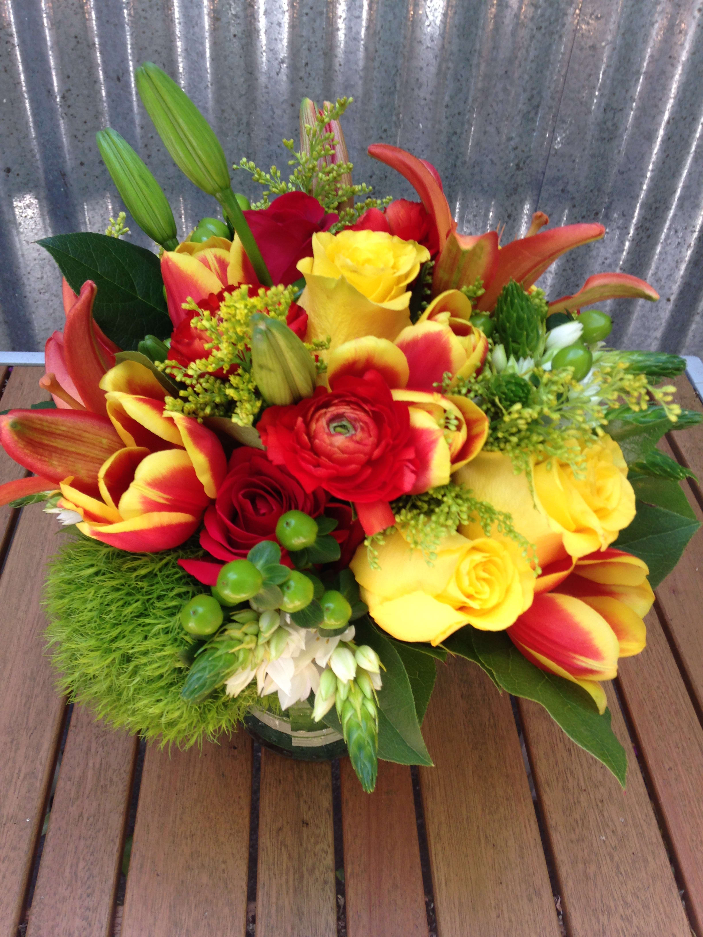 Automntime sunset - This low centerpiece packs a vibrant punch of yellows and orange. Featuring orange lilies, yellow roses, dianthus, hypericum and other seasonal filler. (Some flowers may be subject to change depending on the season. We will contact you with available flower substitutions; please contact us with specific questions if you are concerned with flower availability, thanks!)  Featured Arrangement: $125.50