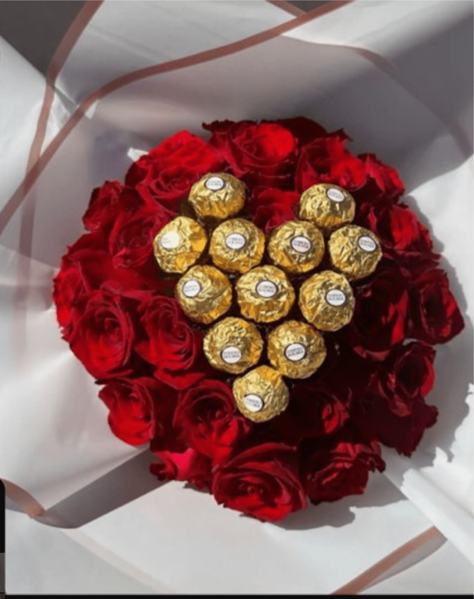 CHOCO BOUQUET - A heart-shaped cluster of velvety red roses set around a gleaming nest of Ferrero Rocher chocolates makes this flower arrangement an irresistible anniversary bouquet or Valentine's Day gift. The rich red roses and metallic-gold chocolates create a striking romantic contrast that reads as both luxurious and celebratory - the perfect way to make the person you love feel cherished.  The arrangement is tightly rounded into a heart-like form and presented in soft white wrapping paper with gentle curved folds for a polished gift look. Deep red rose petals sit close together around several gold-wrapped Ferrero Rocher candies, so the bouquet combines classic floral romance with a sweet, shareable treat.  Arrives compact and ready to present, ideal for surprising a partner on anniversaries, Valentine's Day, or any moment you want to say "I love you" with both flowers and chocolate. Handle with care; keep away from direct heat and sunlight to preserve the roses and chocolates until the moment you gift them.