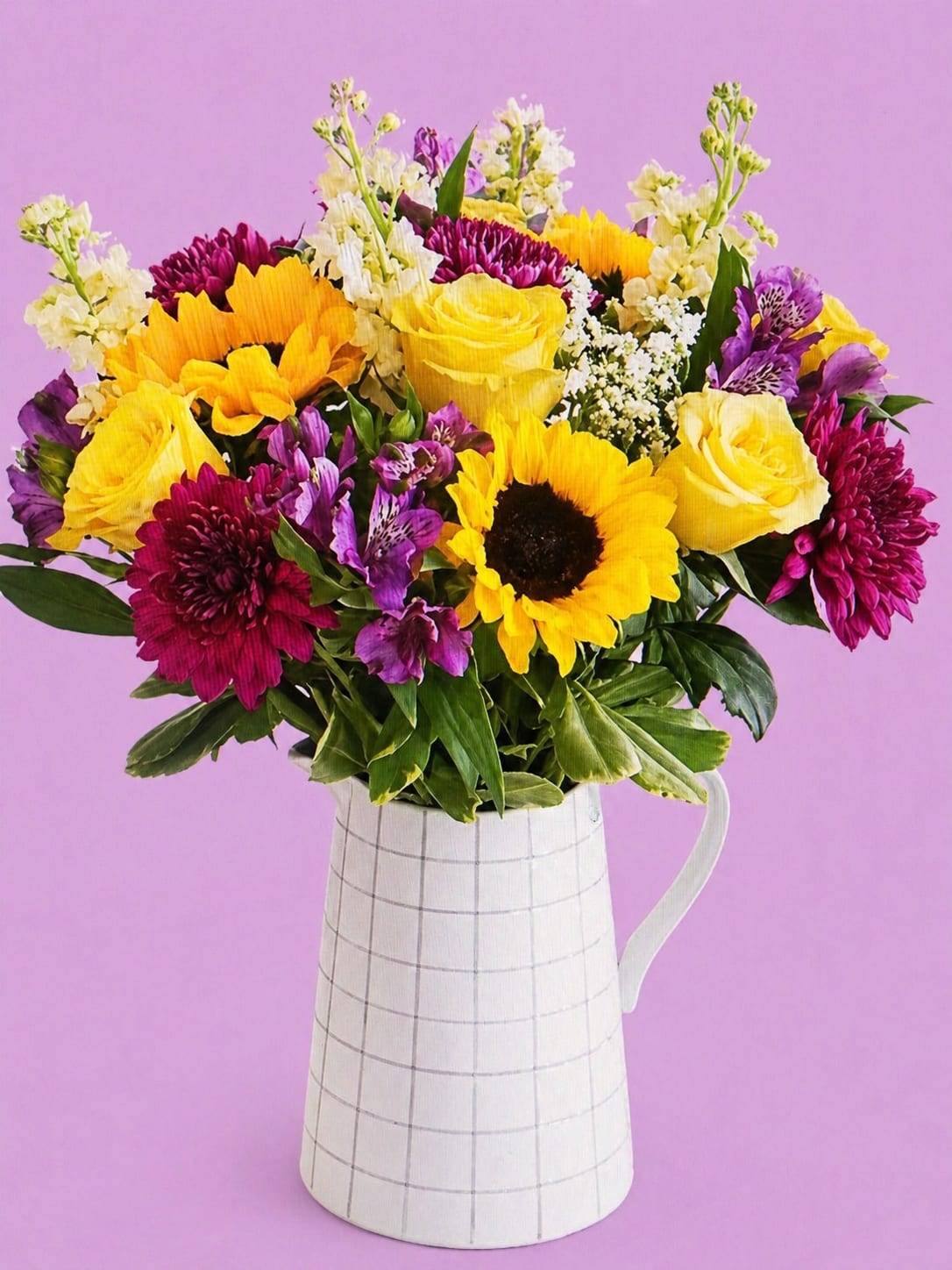 Golden Harmony  - Roses, sunflowers, Peruvian lilies, and more in a lively, lovely palette burst forth from a pitcher-shape vase decorated with a windowpane plaid motif. 