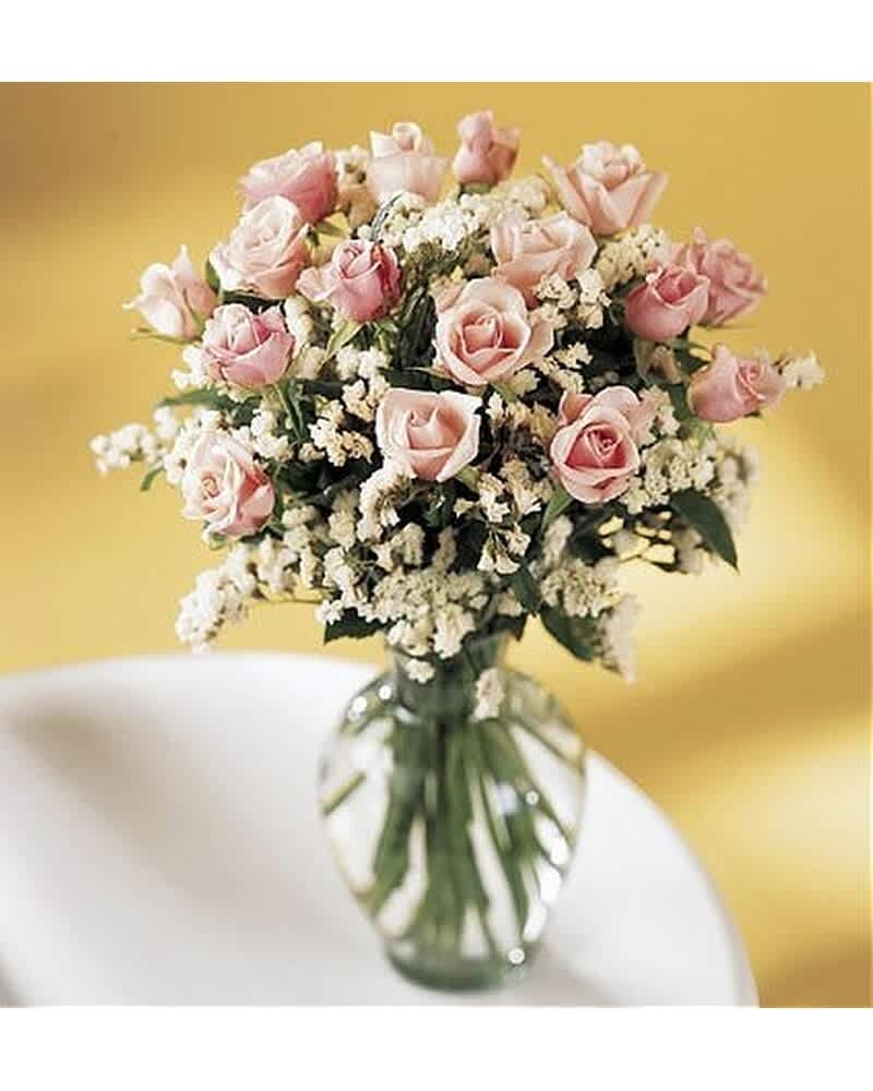 Glass vase of light pink roses with white filler flowers against a yellow background