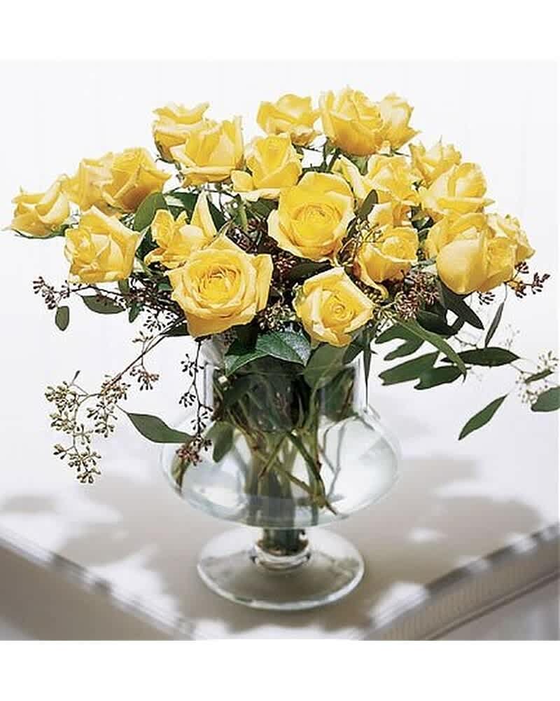Arrangement of yellow roses with filler in a clear pedestal glass vase