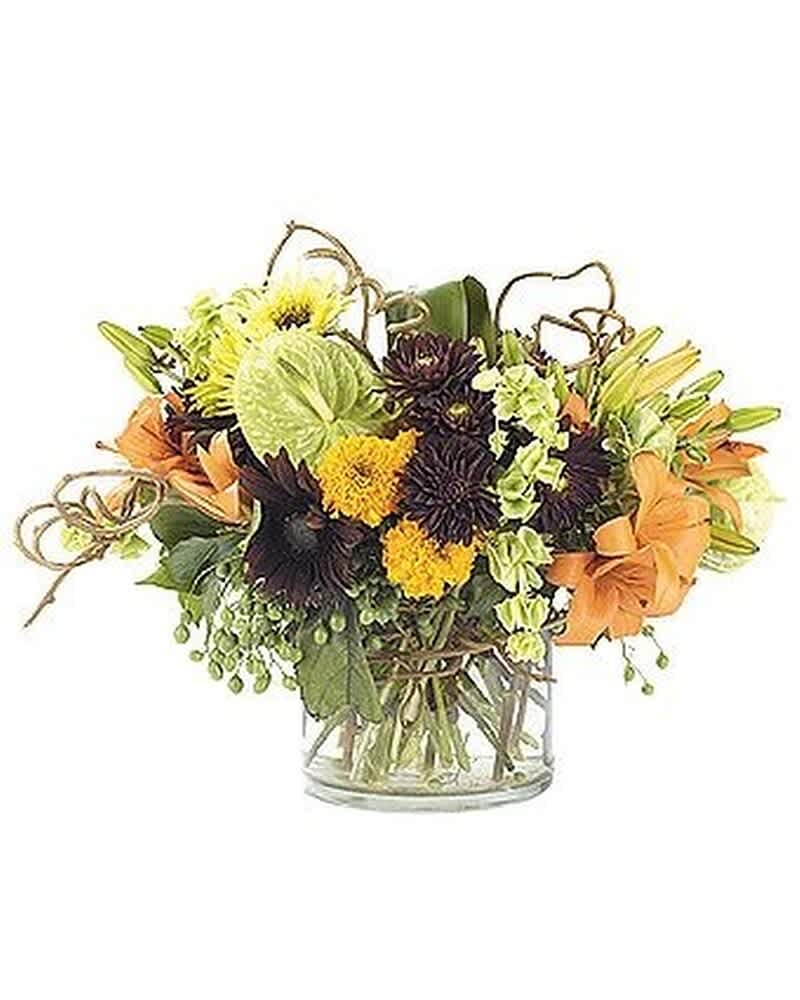 Low arrangement of orange lilies, yellow and dark blooms with green accents in a clear glass vase