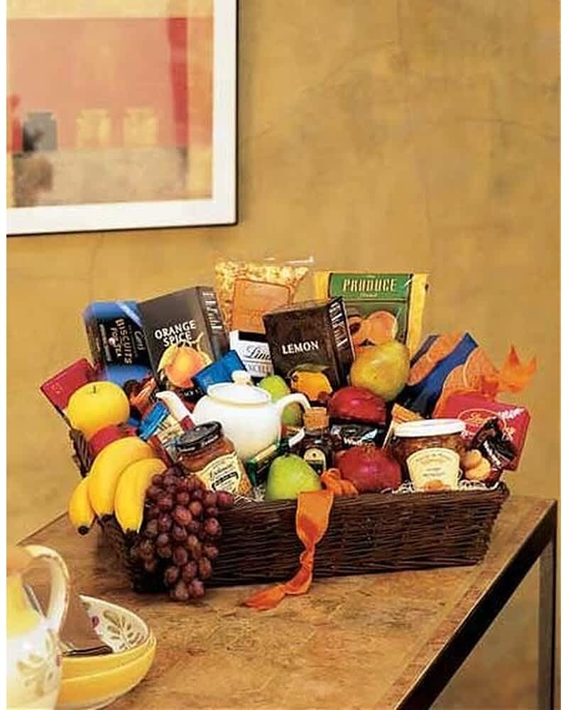 Large wicker gift basket filled with assorted gourmet snacks and fresh fruit on a table