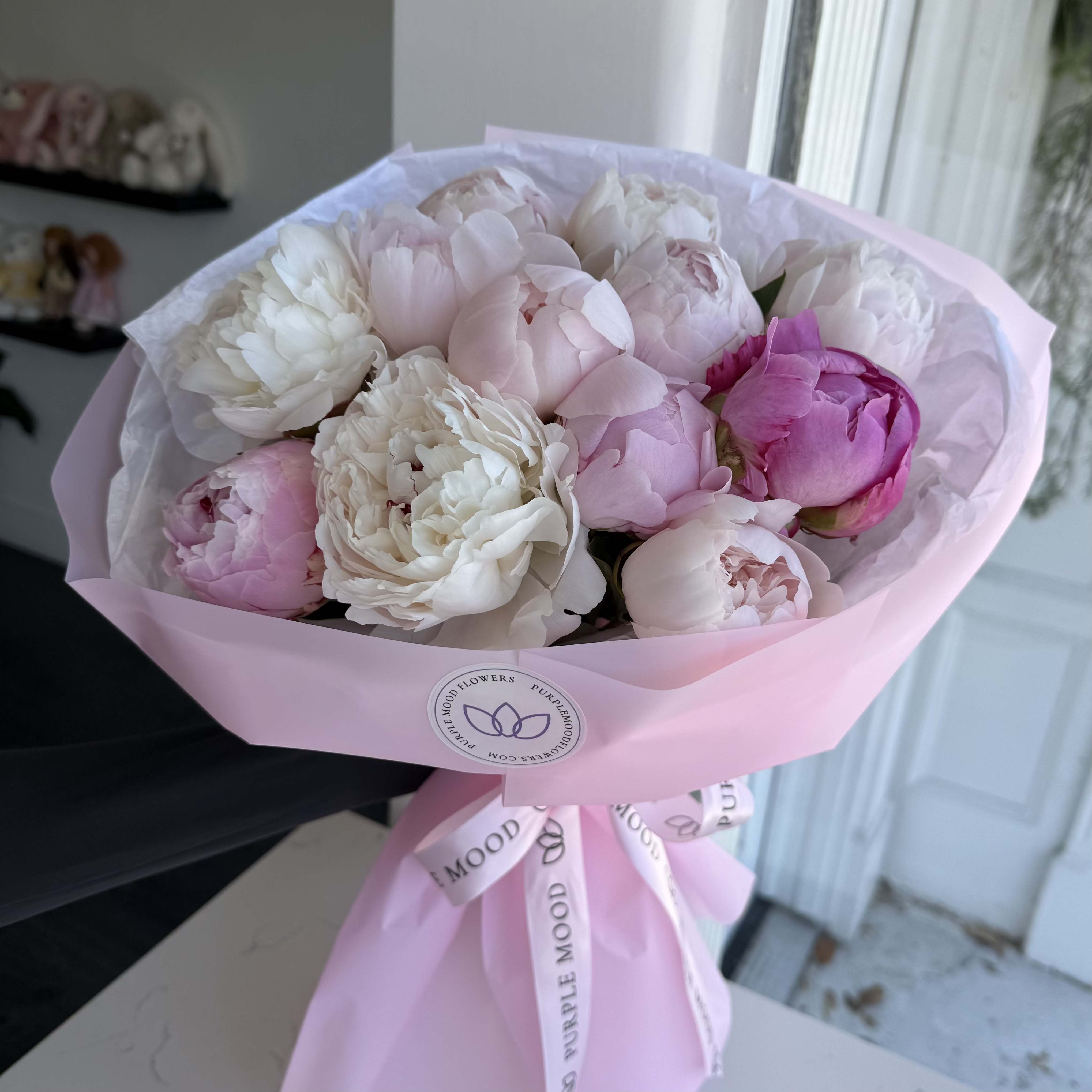 Just Peony Bouquet - A timeless bouquet of lush peonies in soft blush, ivory, and delicate pink tones, beautifully wrapped in our signature pastel packaging. Each bloom is carefully selected for its full, ruffled petals and romantic garden feel, creating an elegant and effortlessly luxurious look.  Perfect for Mother’s Day, birthdays, or simply to say “I love you.”  Sizes:  Standard – approx. 12 stems Deluxe – approx. 24 stems Premium – approx. 36 stems  Details:  Fresh premium peonies in mixed soft pink and white shades Hand-wrapped in waterproof designer paper Finished with Purple Mood signature ribbon Vase not included