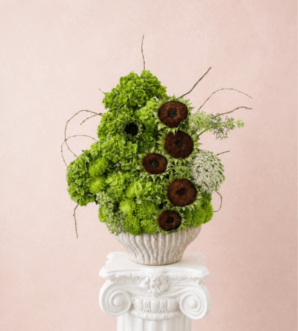 Green floral arrangement with dark sunflower centers in a textured vase