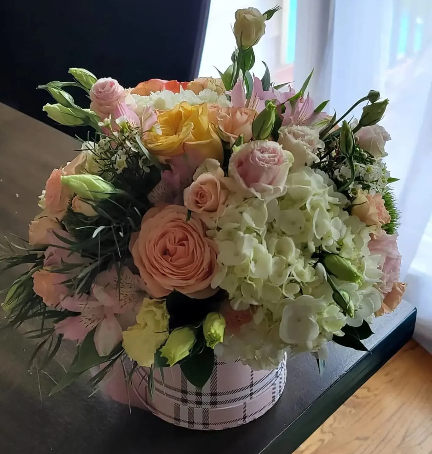 Mixed bouquet of pastel roses and hydrangeas in a plaid round box