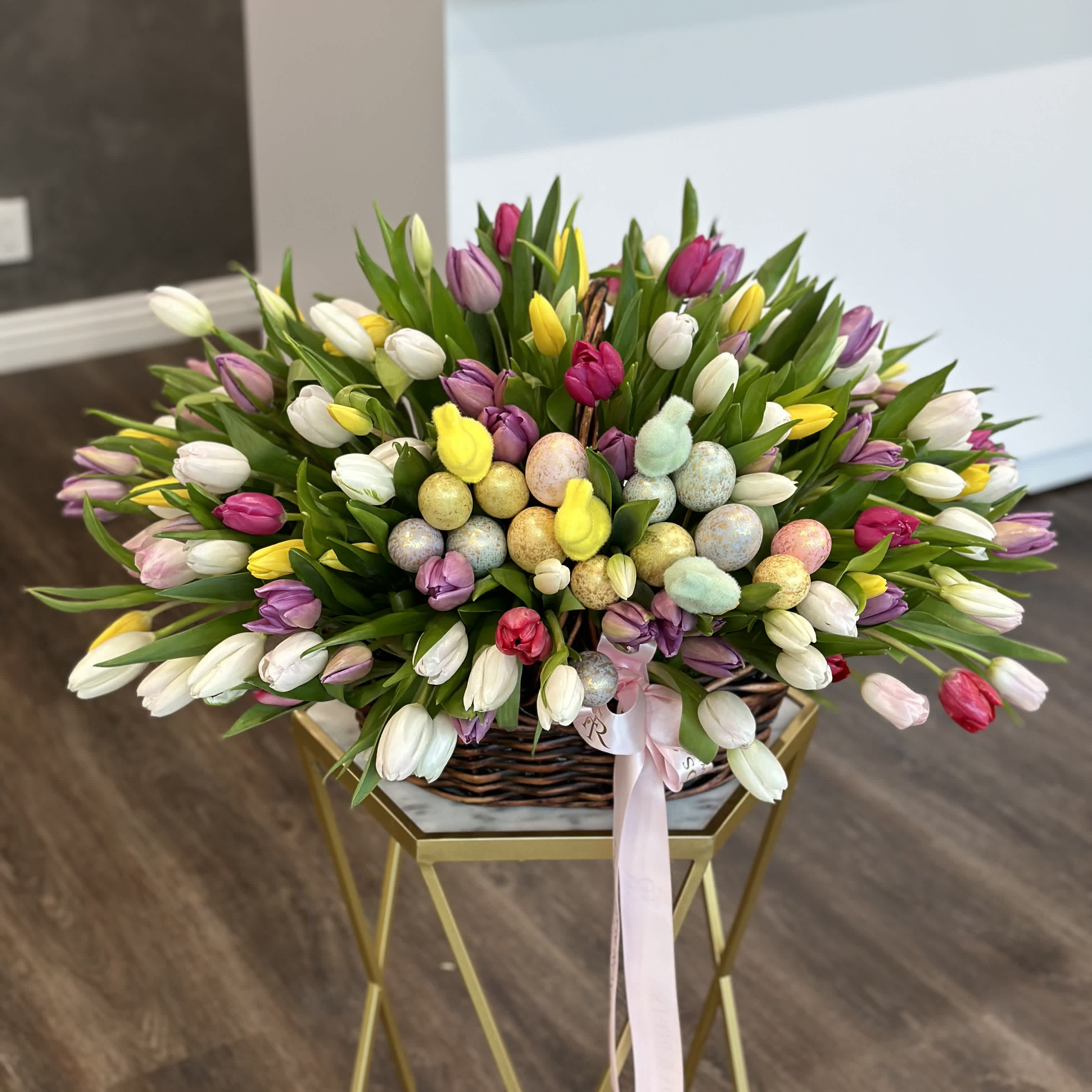 Basket of multicolored tulips with pastel Easter eggs and a pink ribbon