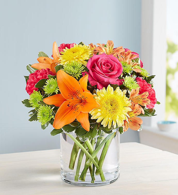 Bouquet of orange lilies, pink roses, and yellow daisies in a clear glass vase
