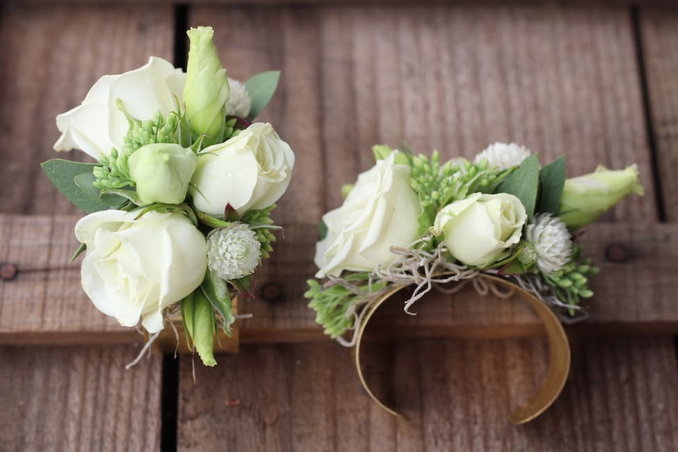 White rose wrist corsage with green accents on a band