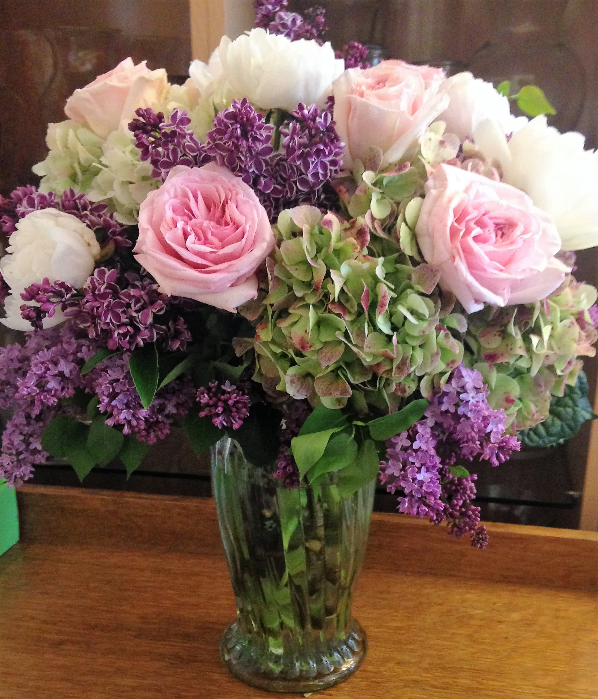Pink roses and white blooms arranged in a clear glass vase with purple flowers
