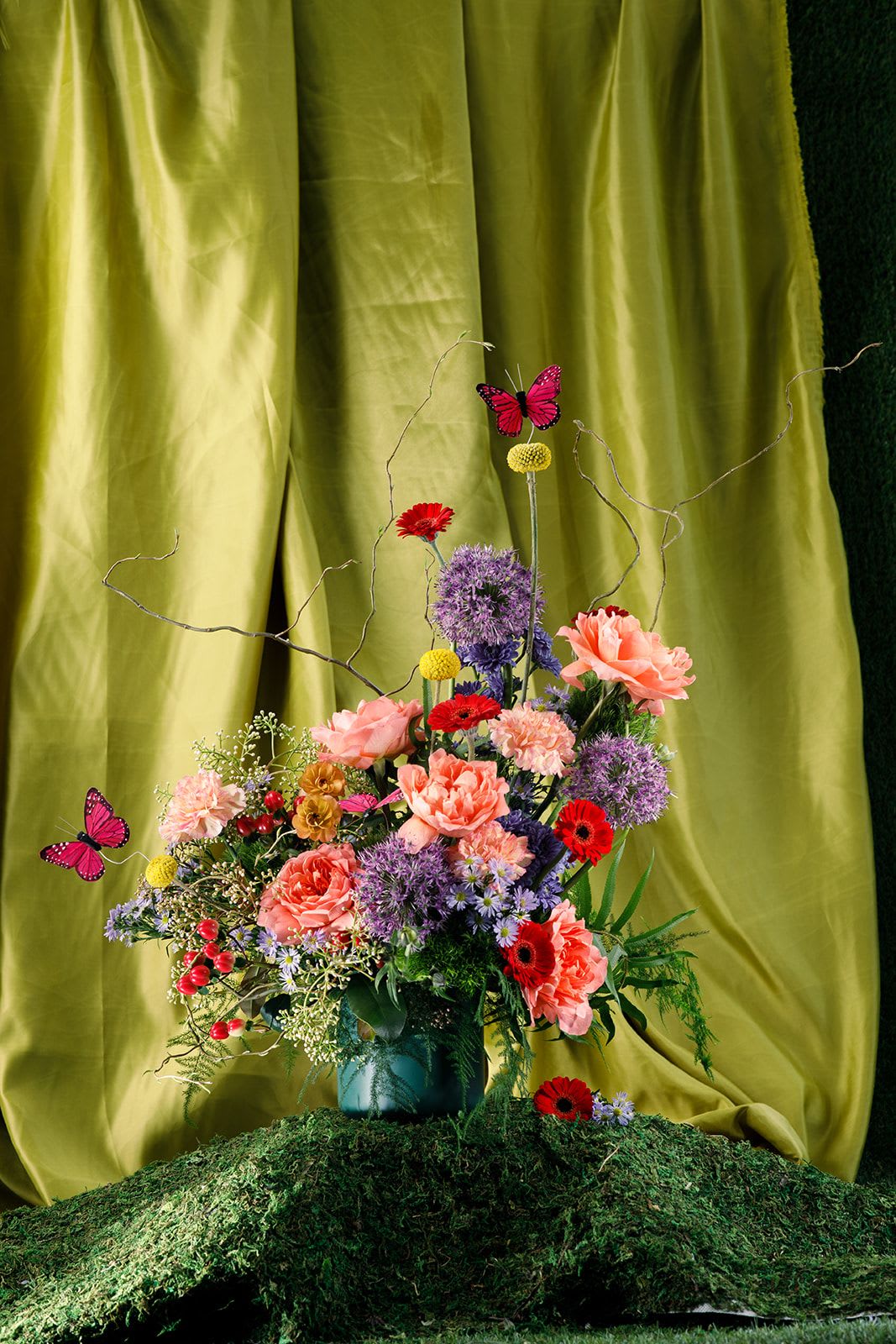 Ladies of the Garden - Ms. Butterfly  - The Transformation Mother  Bursting with color and movement, Ms. Butterfly is a joyful expression of growth, beauty, and becoming. Designed in a vibrant mix of seasonal blooms, this arrangement features Dragonfly roses, bright red micro gerbera daisies, and soft lavender aster—creating a contrast that feels both playful and elevated.  Layered with white wax flower, golden billy balls, ranunculus, hypericum berries, and curly willow, the bouquet is tightly gathered for a full, textural silhouette with a touch of whimsy—like a garden in motion.  Hand-tied and ready to display, this piece honors the mother who nurtures every stage—trusting that all she’s poured in will one day take flight.  To keep your blooms fresh, trim stems and refresh water every two days.   Please note that this is an exclusive collection for Mother's Day, May 8-10. 