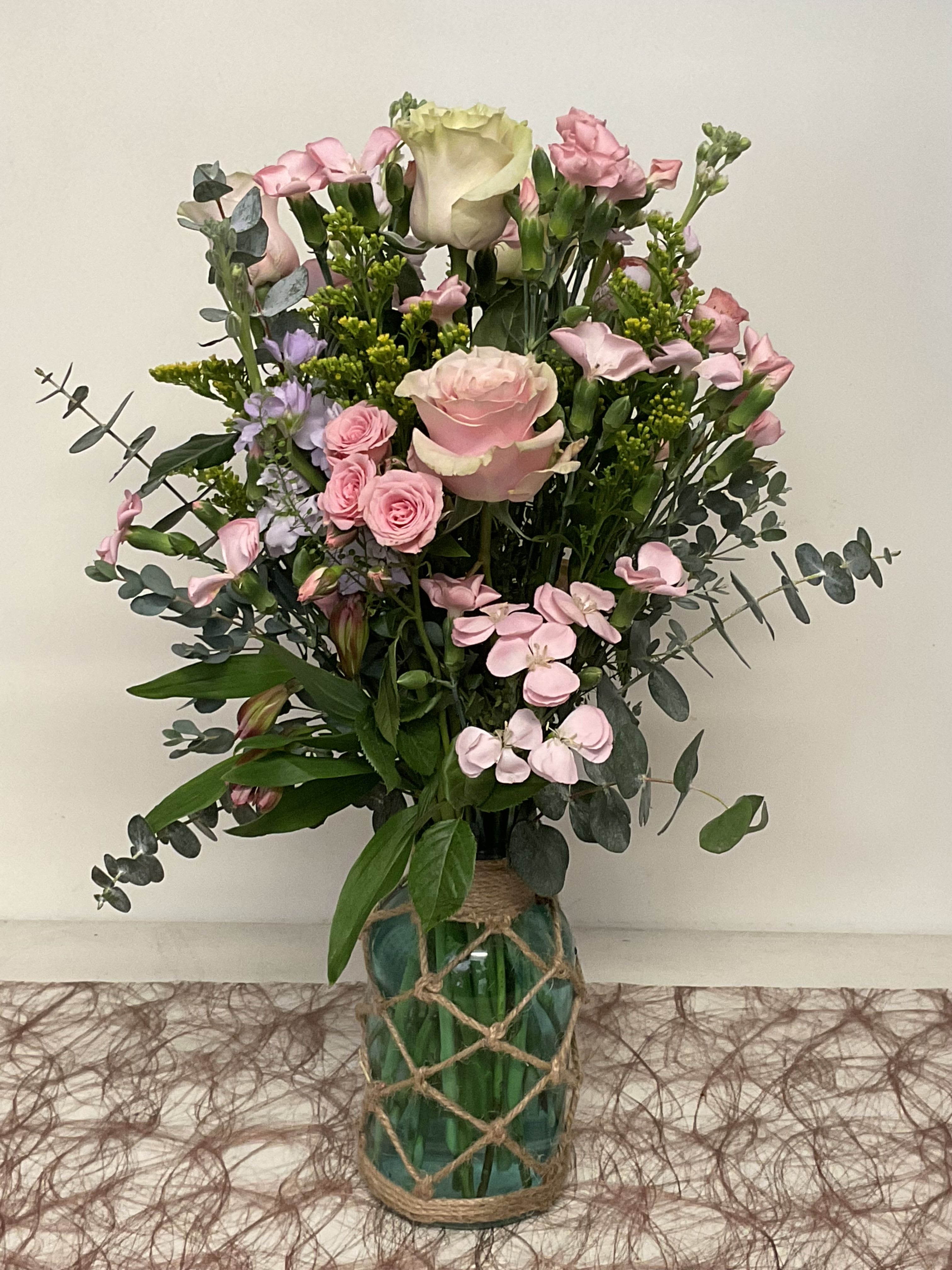 26-126 - Tall, garden-style mix of pink roses, spray roses and mini carnations in glass vase wrapped with rope.