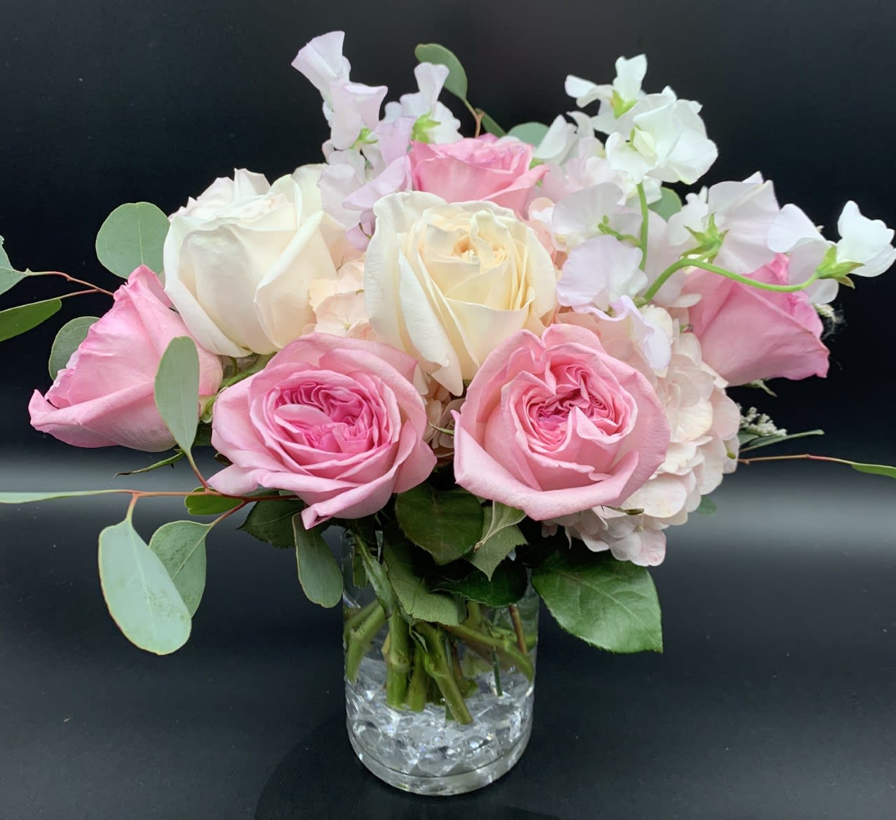 Compact arrangement of pink and cream roses with soft blush blooms in a clear glass vase.