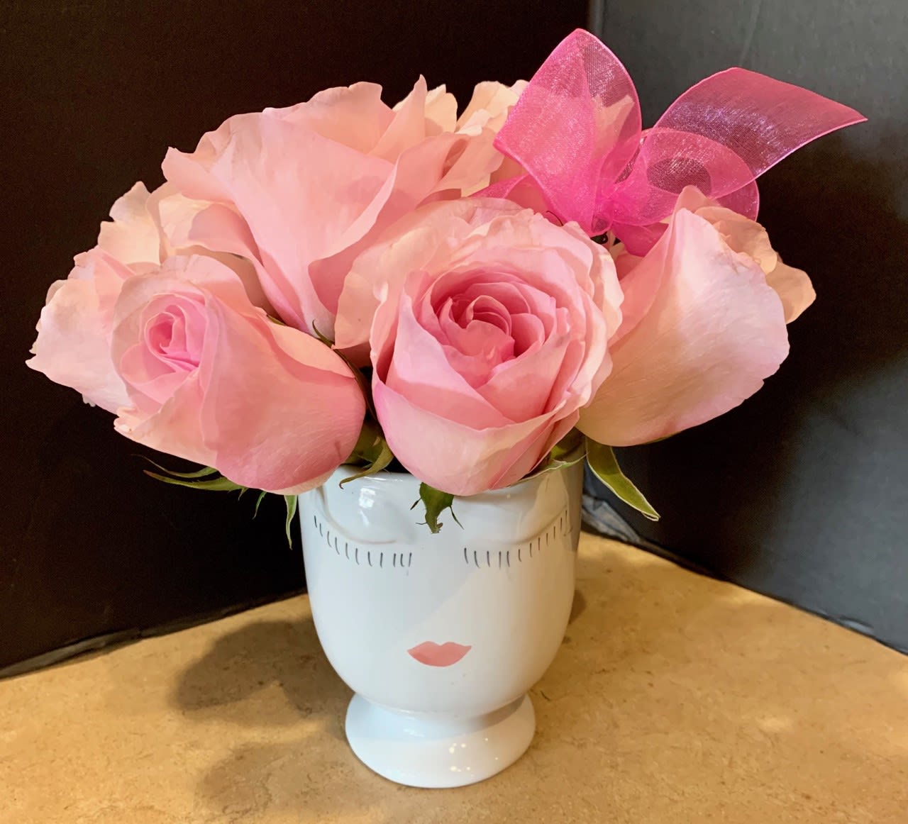 Pink roses arranged in a white face-shaped vase with a pink bow