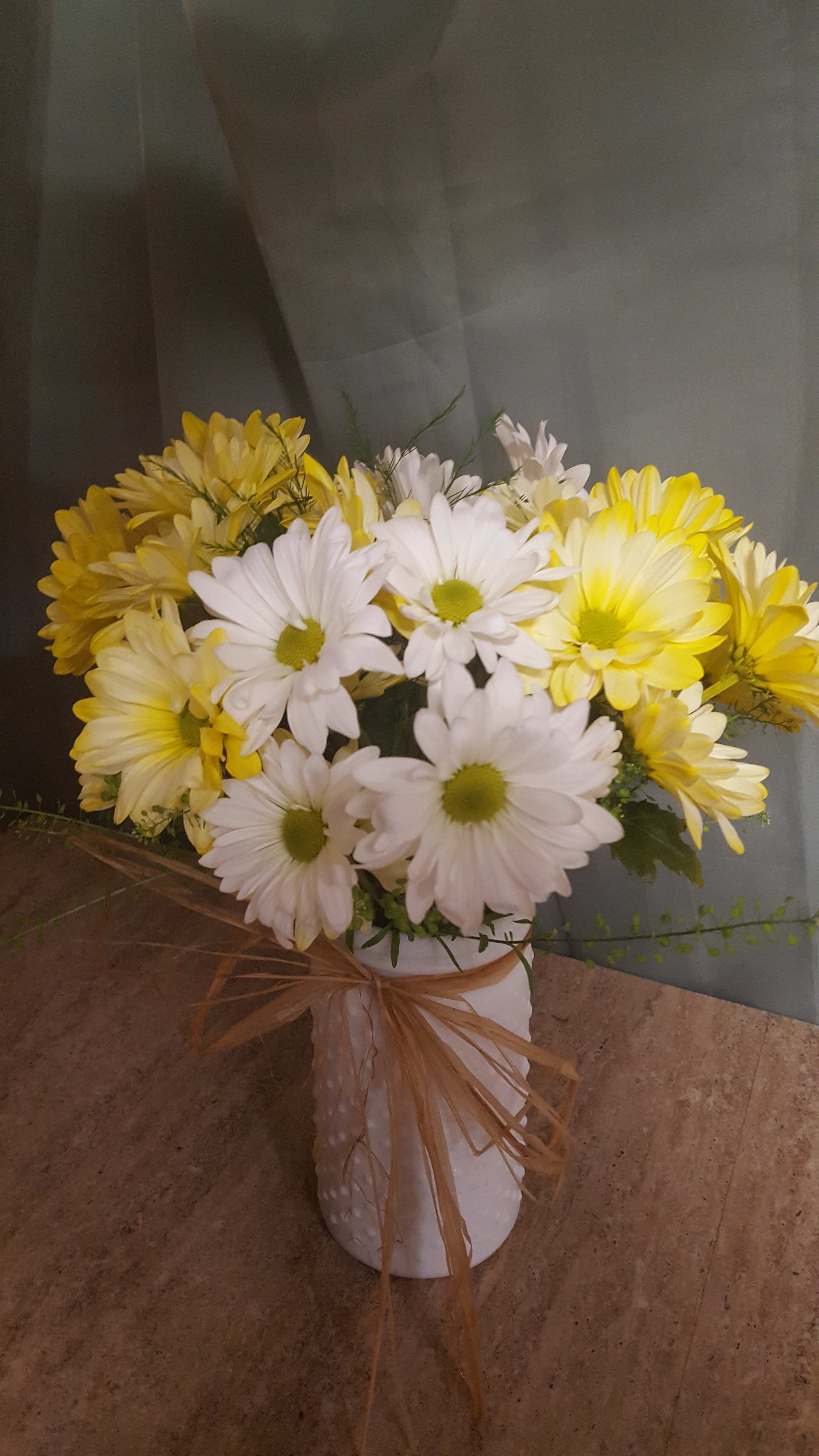 Yellow and white daisy bouquet in a white vase with a ribbon