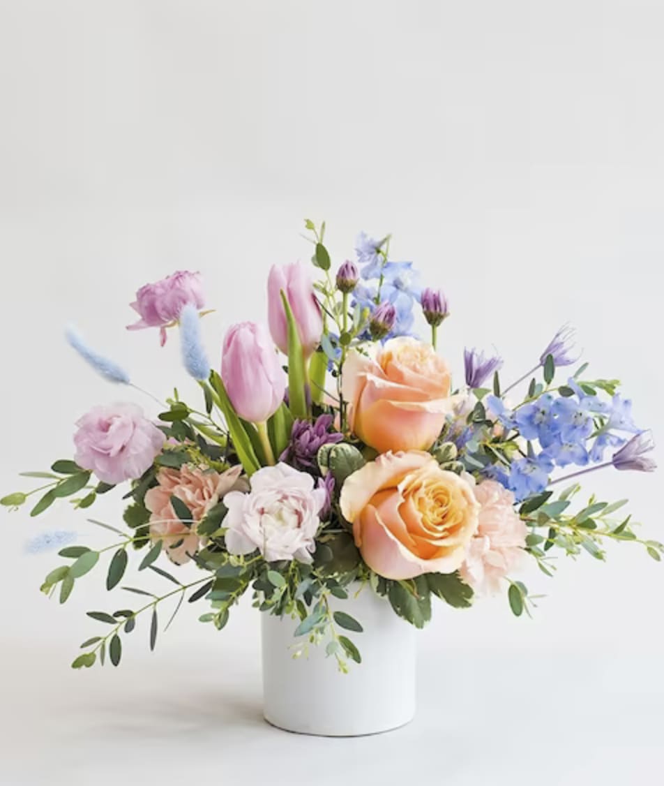 Pastel bouquet of roses, tulips, and blue flowers in a white vase
