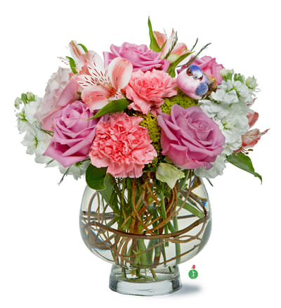 Round arrangement of pink roses, carnations, and white blooms in a clear glass bowl vase